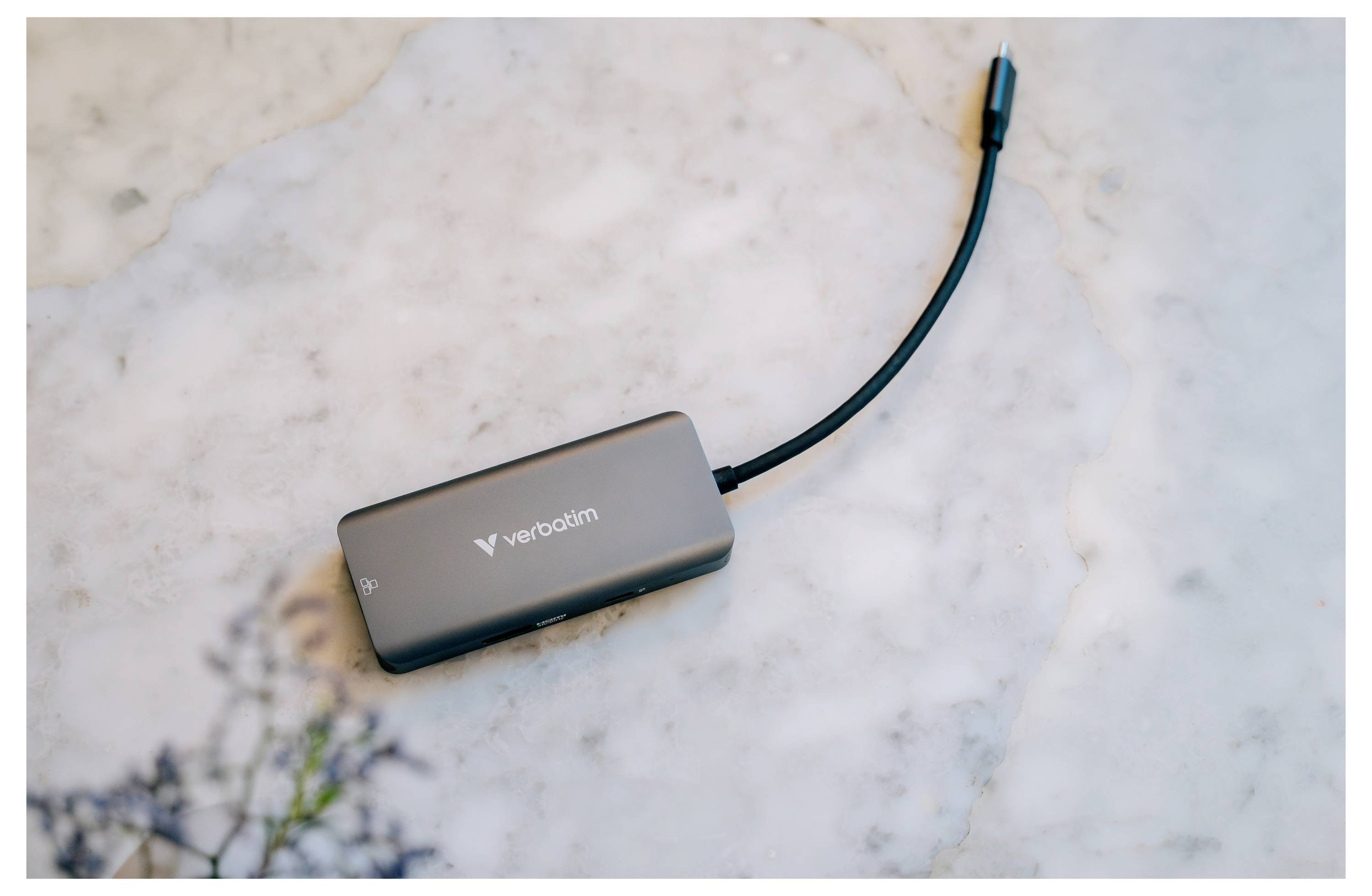 Černý rozbočovač Verbatim USB-C s připojeným kabelem leží na světlém mramorovém povrchu.