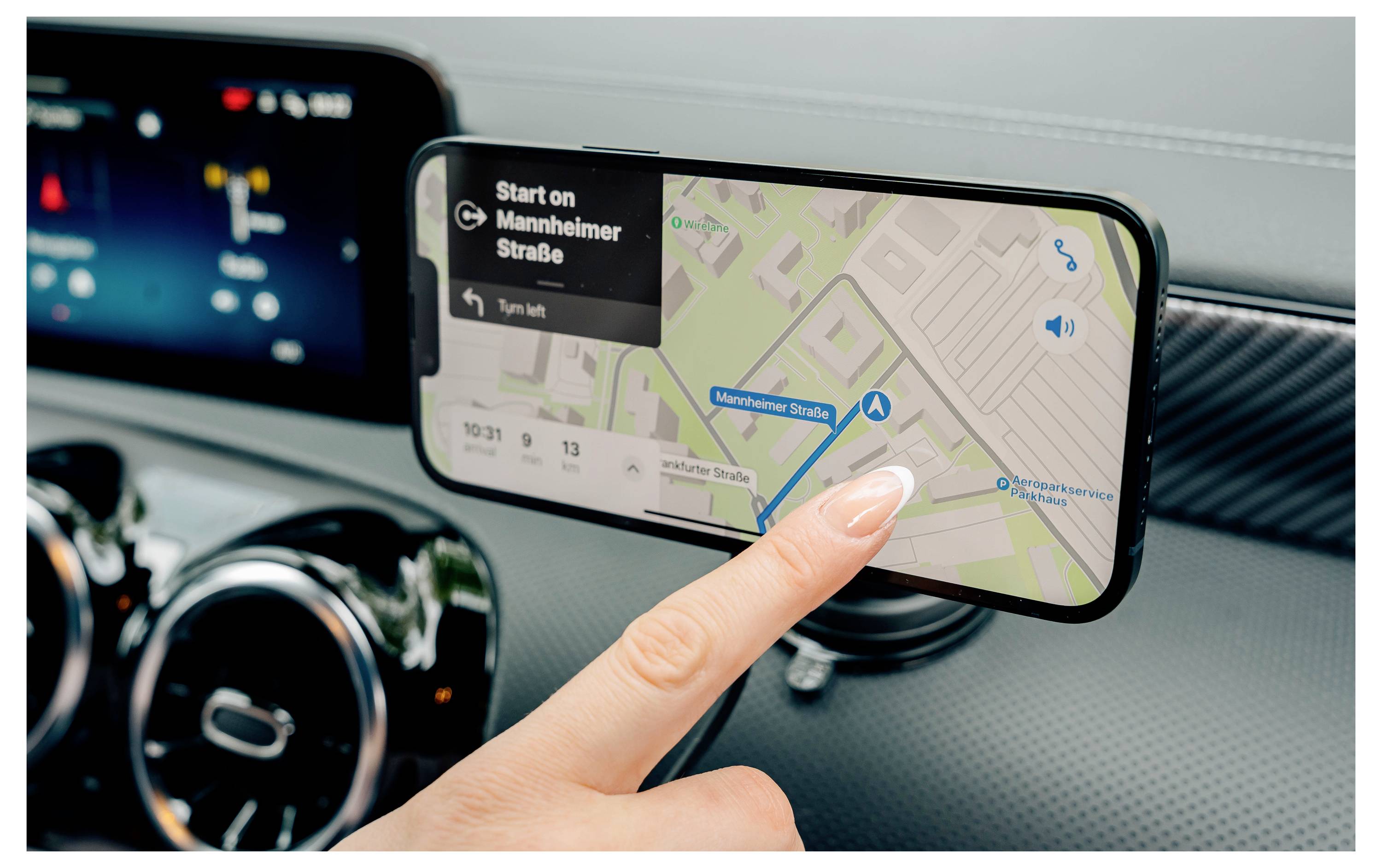 Osoba používající smartphone upevněný na palubní desce automobilu pro navigaci, zobrazující mapu se směry zatáčení po zatáčce na Mannheimstraße.