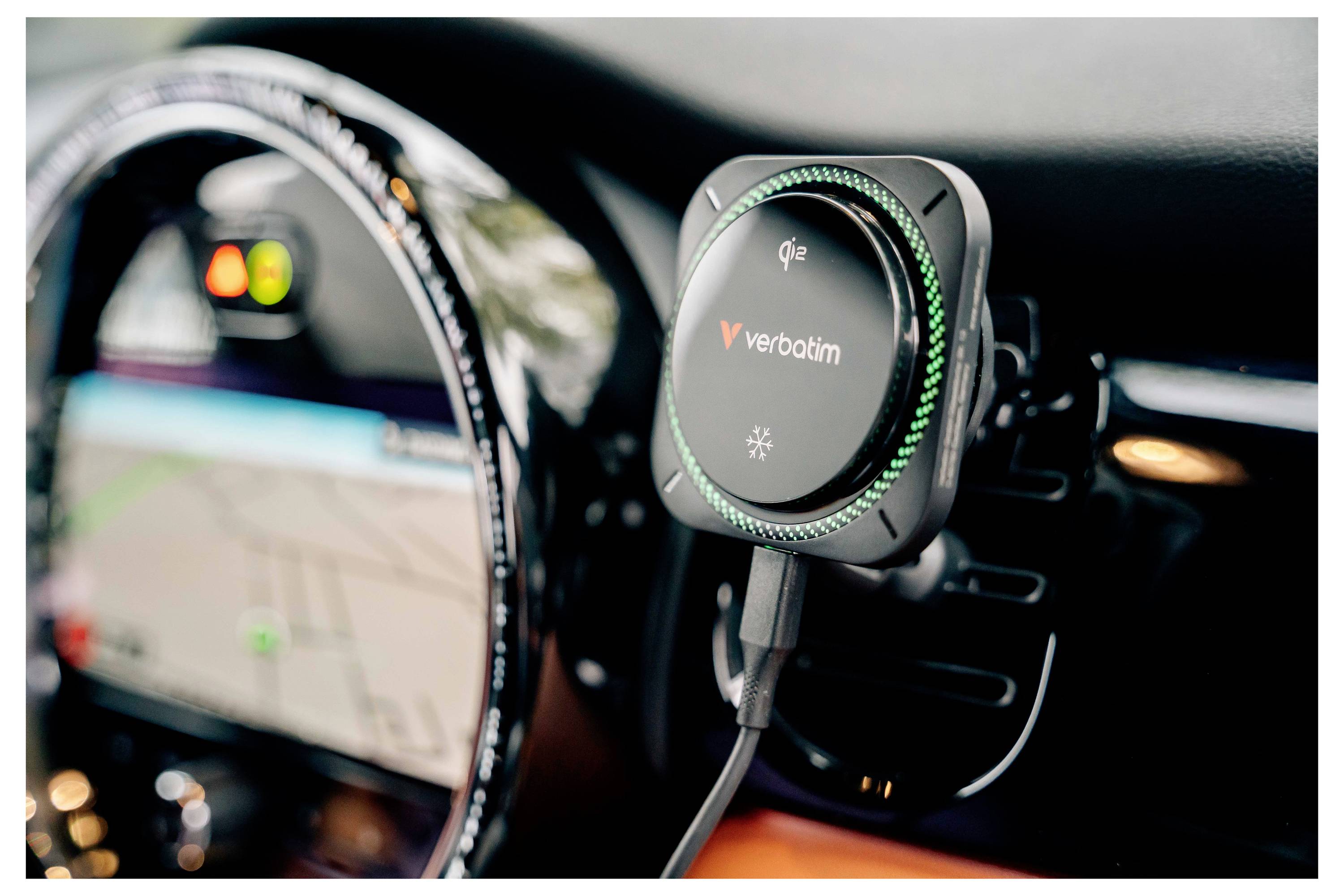 Bezdrátová nabíječka mobilního telefonu Verbatim Qi připevněná na přístrojové desce automobilu s připojeným kabelem a rozmazaným přístrojovým štítem v pozadí.