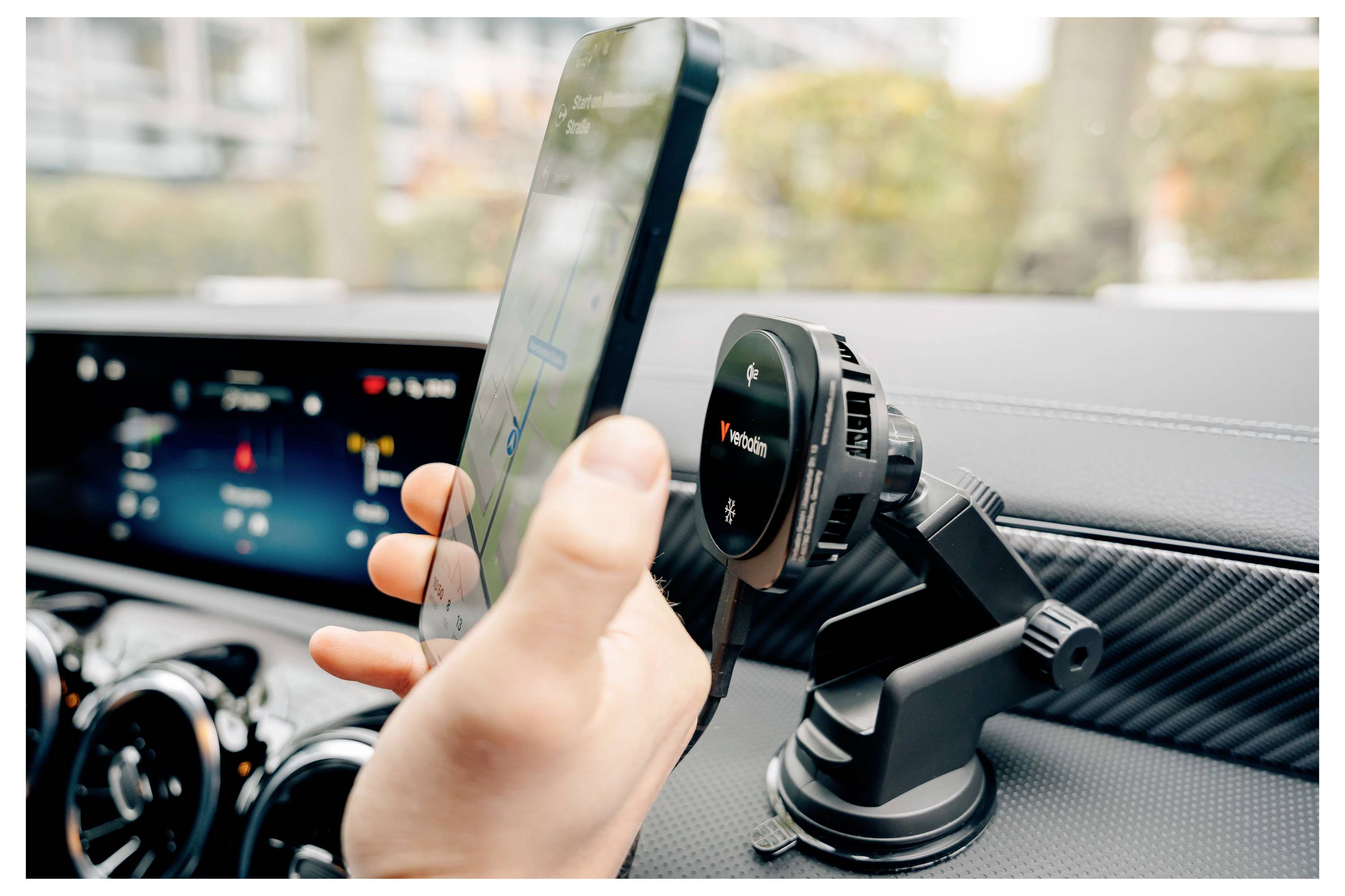 Ruka drží chytrý telefon blízko držáku telefonu v automobilovém přístrojovém panelu, zobrazující navigaci v autě nebo nastavení.