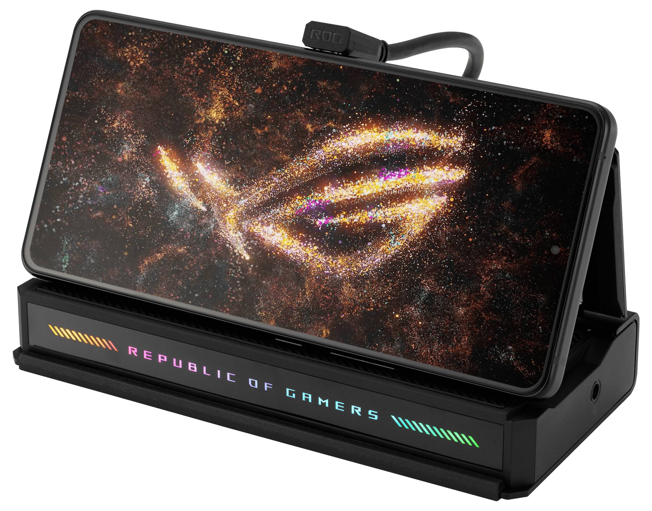 'Smartphone zobrazující logo Republic of Gamers v zářících částicích, umístěný na černém stojanu s barevnými LED světly.'