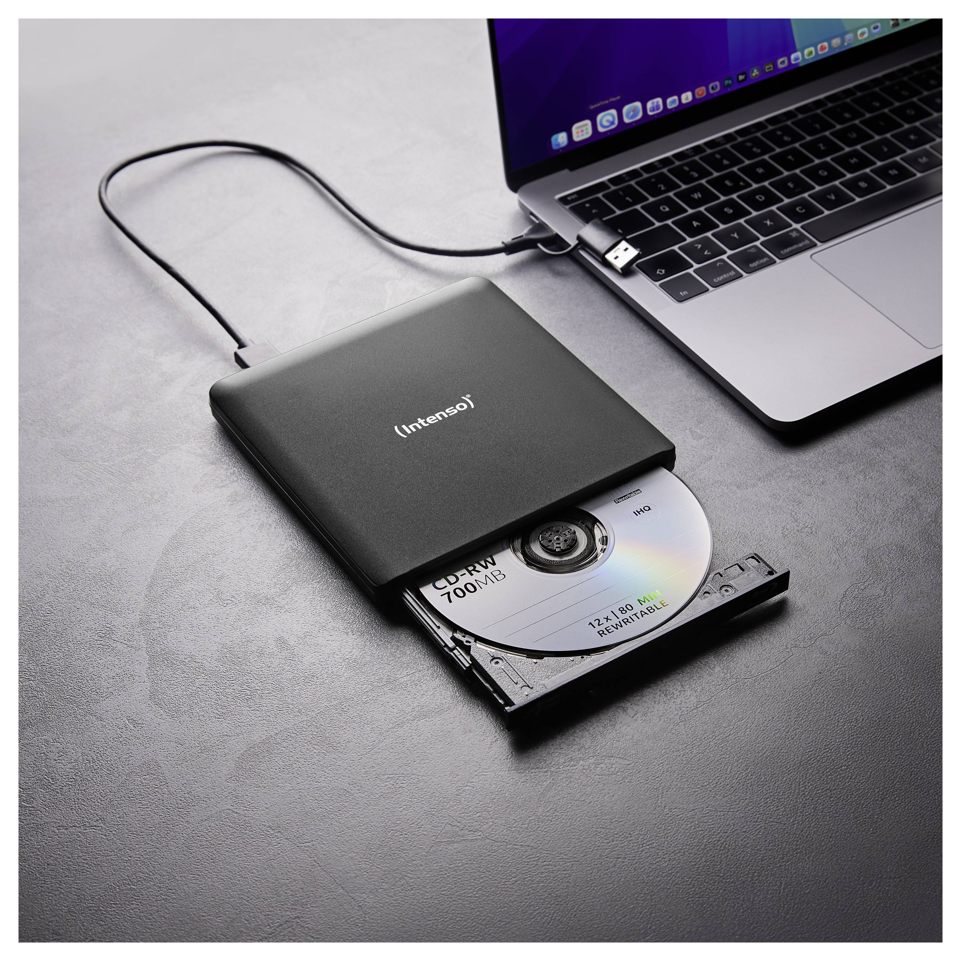 Externí jednotka CD/DVD připojená k notebooku s částečně vloženým CD. Notebook a jednotka spočívají na šedém povrchu.