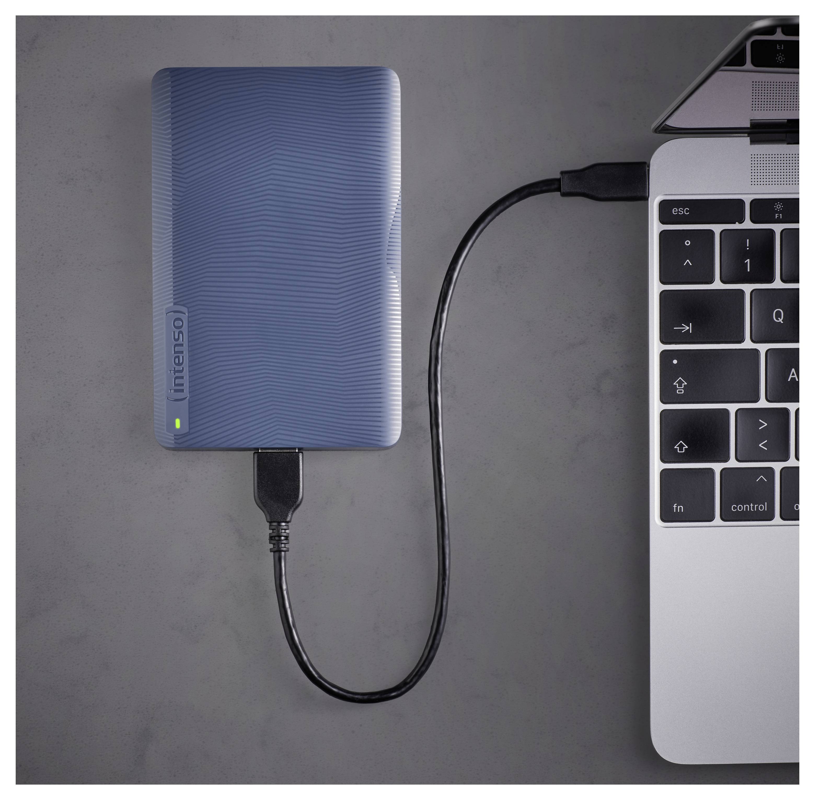 Externí pevný disk připojený k notebooku přes kabel USB, indikující přenos dat nebo zálohování.