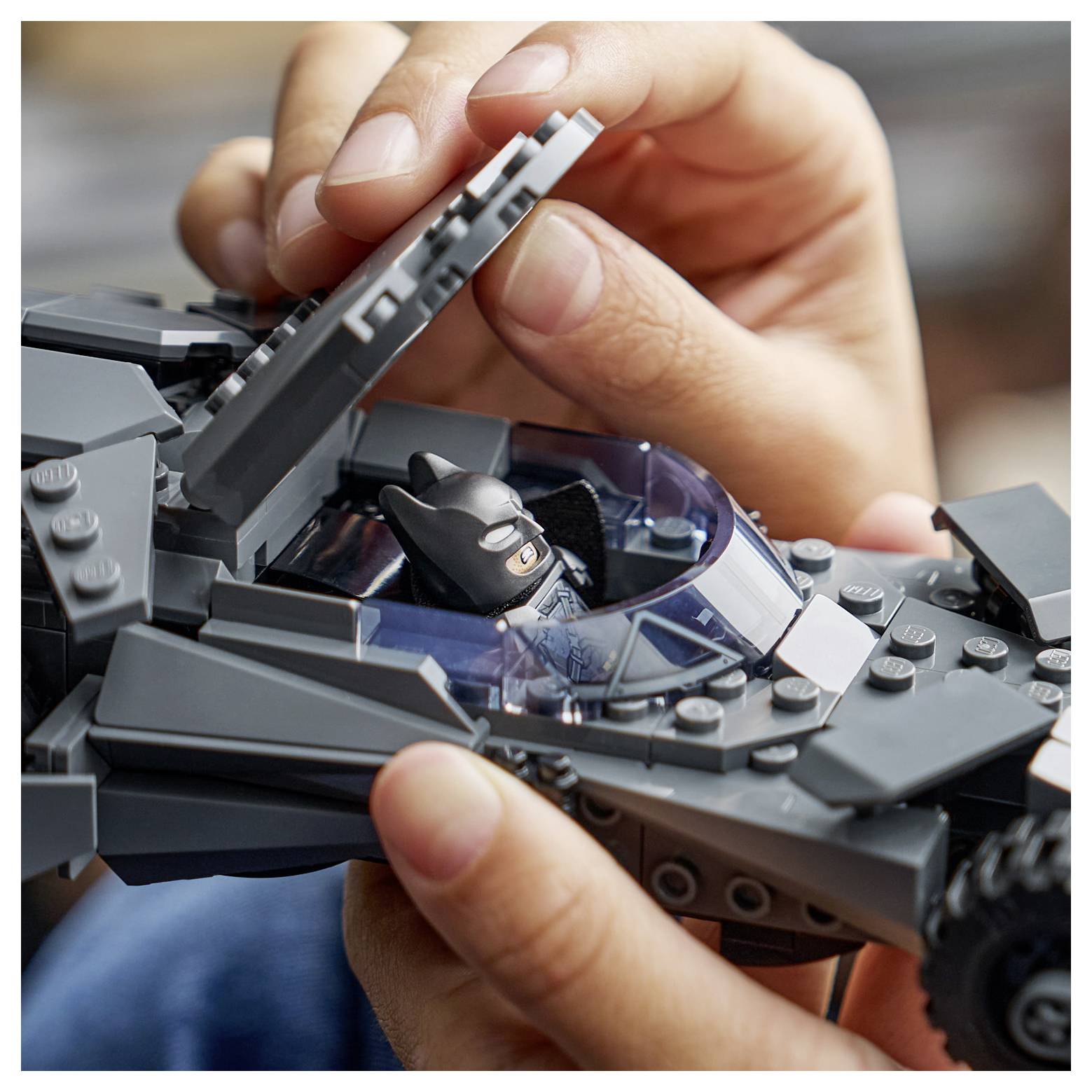 Ruce umisťující figurku "LEGO Batman" do šedého, detailně zpracovaného modelu LEGO Batmobilu, zdůrazňující montáž a hraní.