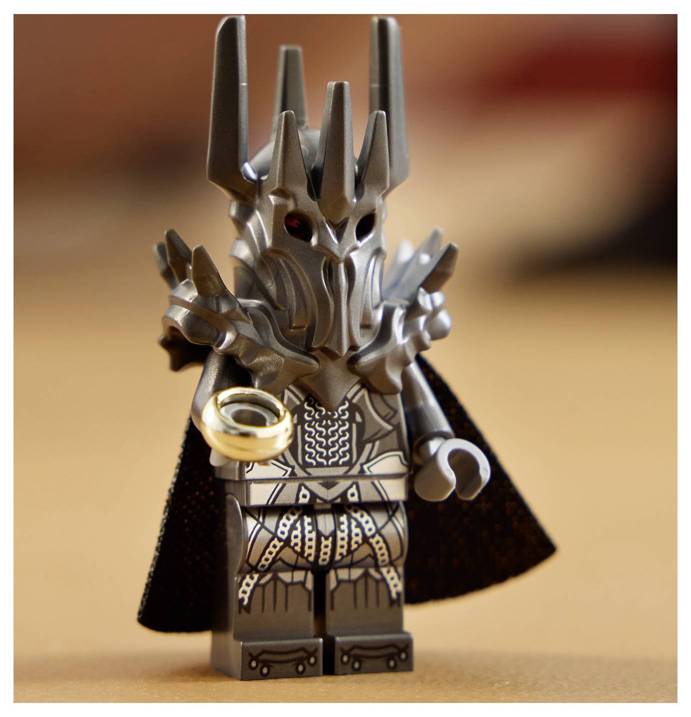 Figurka hračky tmavě oděného postava s hrozivou helmou držící zlatý prsten na rozmazaném pozadí.