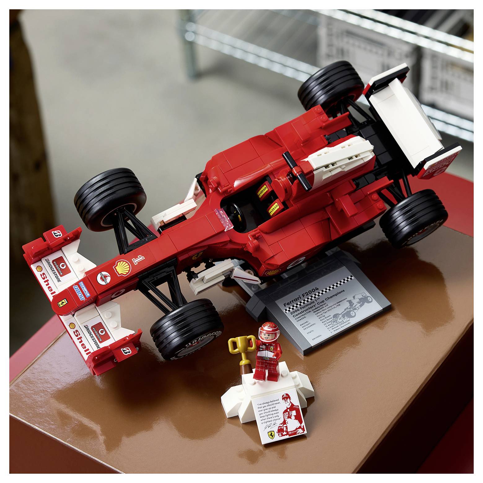 Detailní červenobílý model závodního automobilu z LEGA na výstavě s malou figurkou a cedulí.