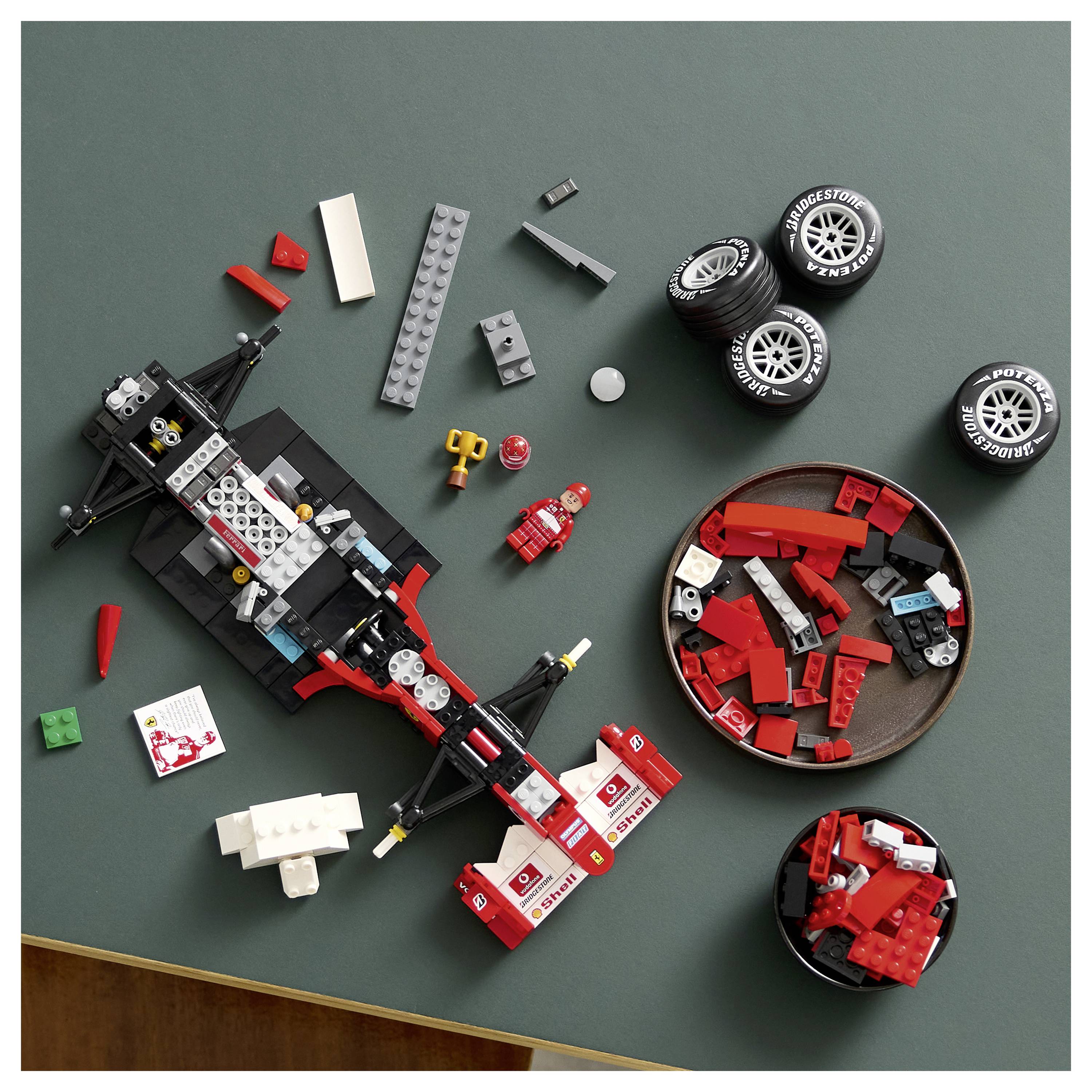Rozebratý červeno-černý hračkářský závodní vůz s díly a čtyřmi pneumatikami uspořádanými na tmavém podkladu, ukazující různé součásti automobilu.