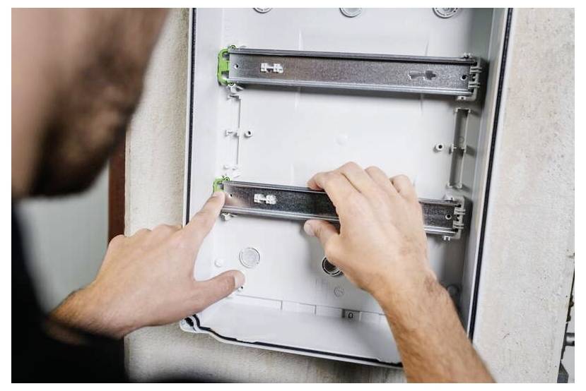 Osoba instalující nebo upravující posuvné kolejnice uvnitř závěsné skříně nebo elektrického panelu