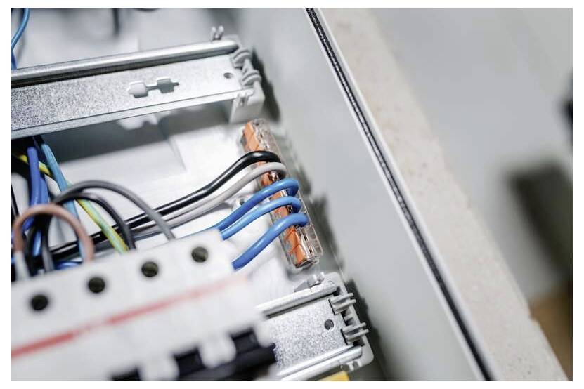 Detailní snímek elektrického zapojení v rozvaděči pojistek, zobrazující modré, černé, zelené a žluté kabely připojené k svorkovnicím.