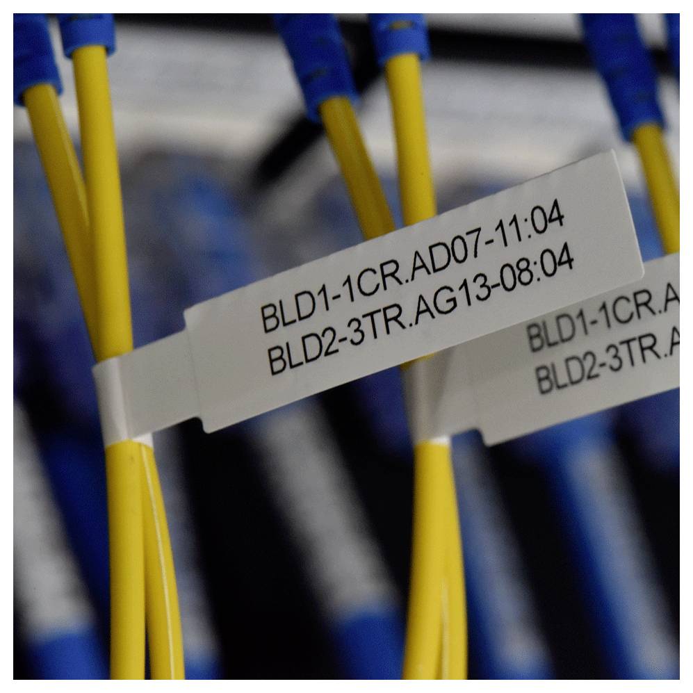 Žluté síťové kabely s bílými štítky s textem „BLD1-1CR.AD07-11:04" a „BLD2-3TR.AG13-08:04" v prostředí serverovny.