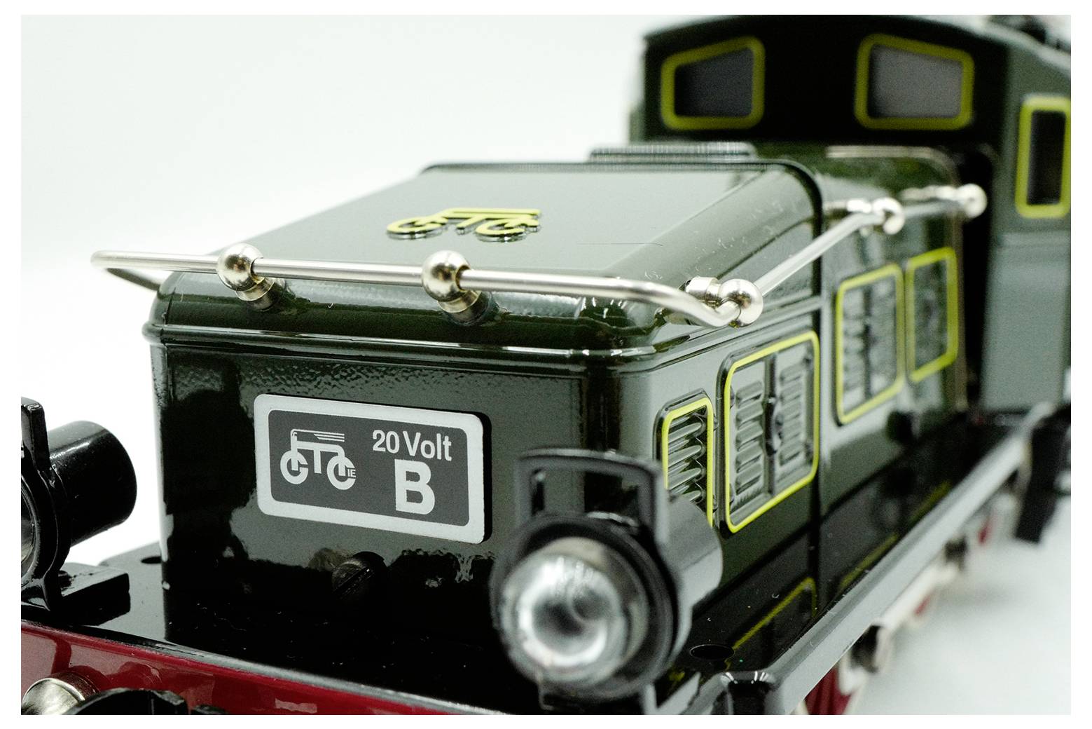 Detailní snímek zelené modelové parní lokomotivy s nápisem "20 Volt B" a symbolem kola na boku, které ukazuje složitost detailů a řemeslnou zručnost.
