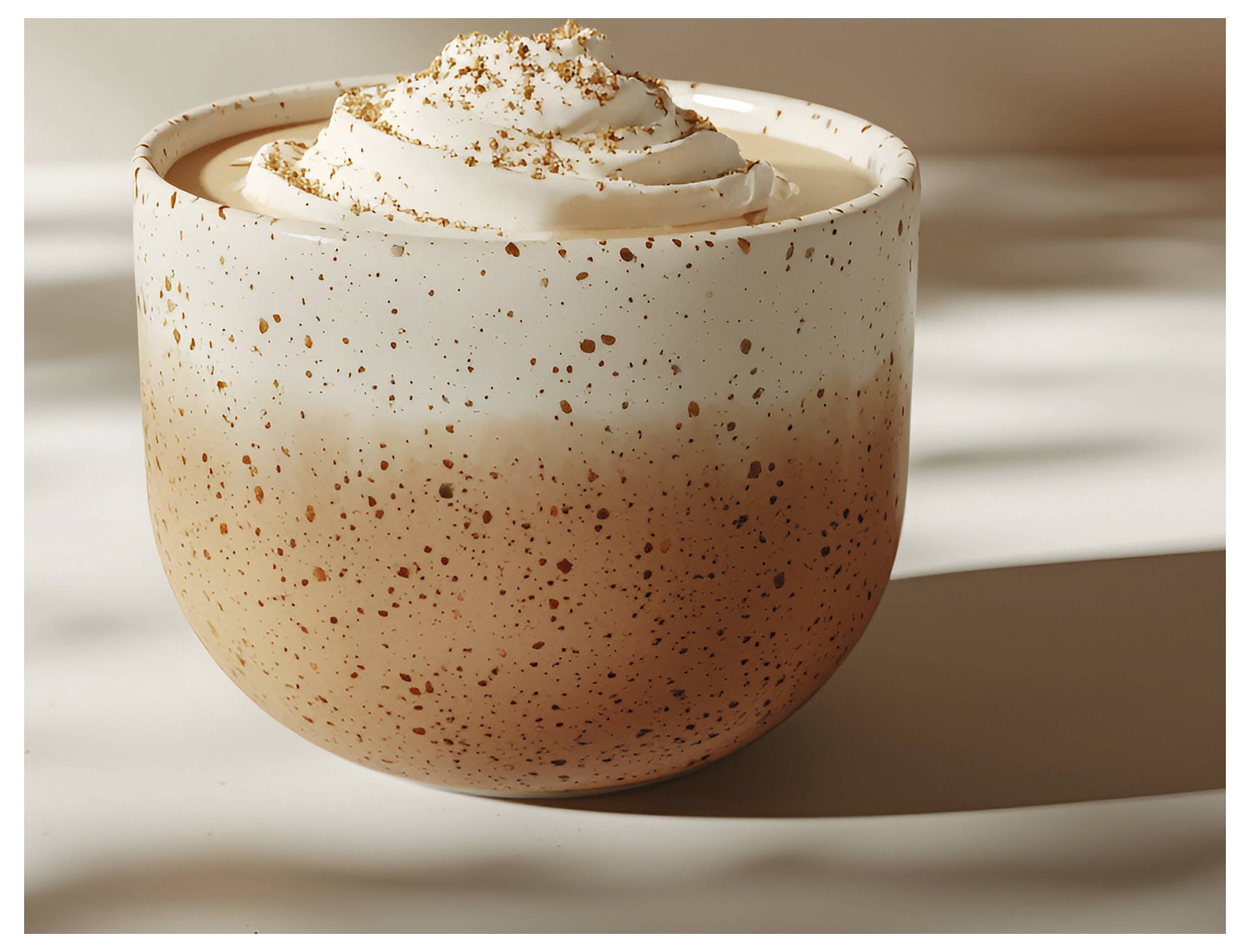 Keramický hrnek naplněný krémovým, pěnivým nápojem s vrcholem zdobeným vířením šlehačky a posypaný skořicí.