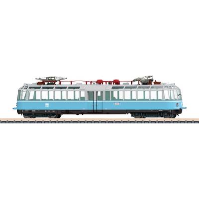 Modrý vintage model železničního vozu se zjednodušeným designem, opatřený velkými okny a horním elektrickým vybavením, vystavený na trati.
