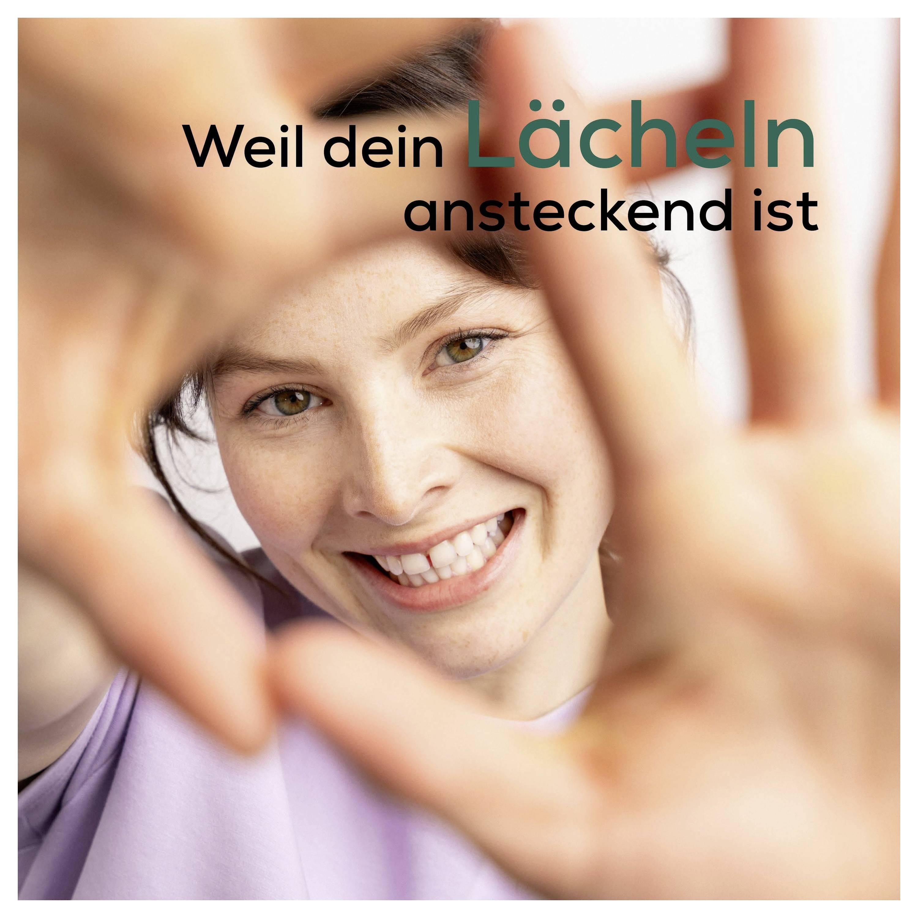 Usmívající se žena si rámuje tvář rukama; německý text říká "Weil dein Lächeln ansteckend ist" ("Protože tvůj úsměv je nakažlivý").