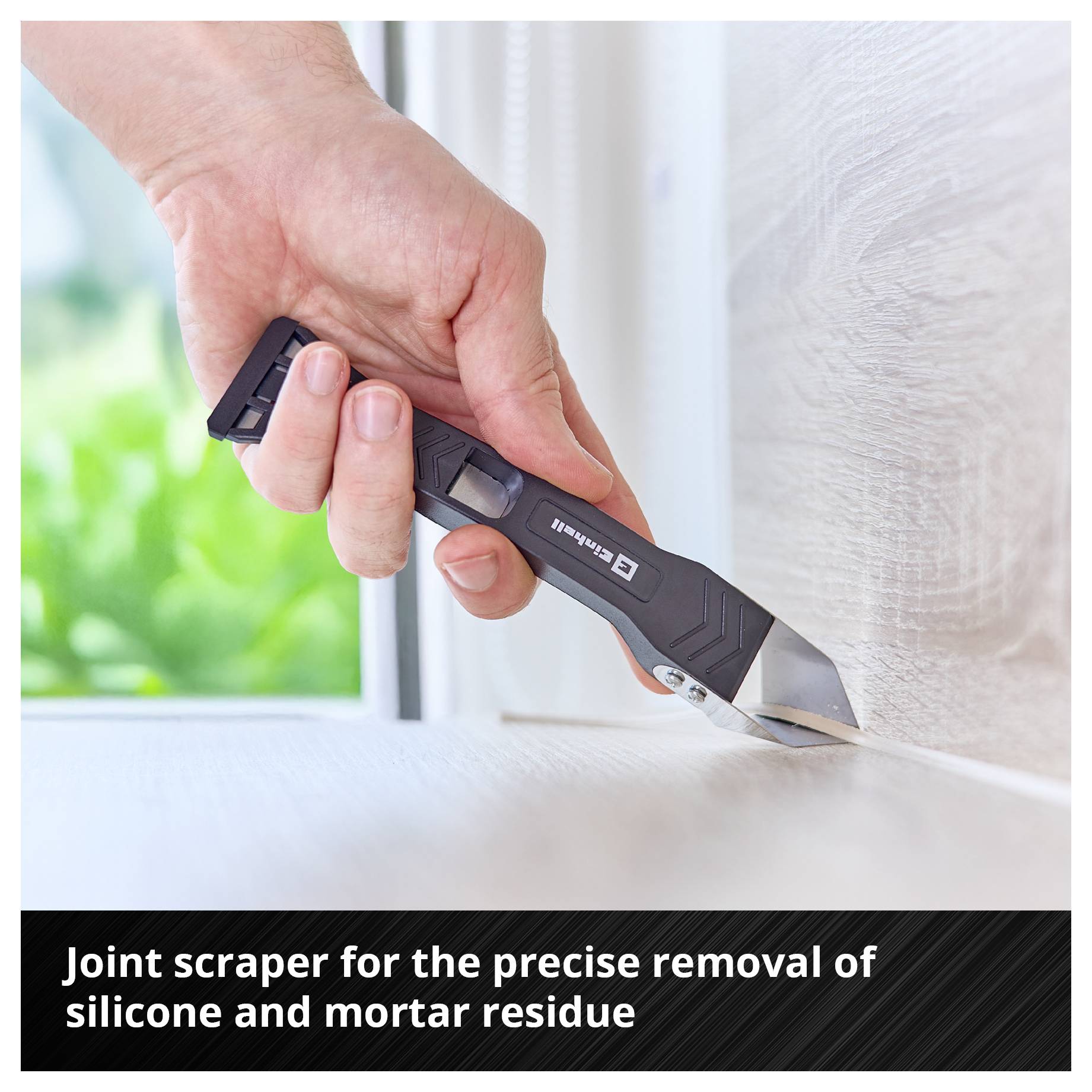 Ruka drží špárovací škrabák a odstraňuje zbytky silikonu a malty z hrany.