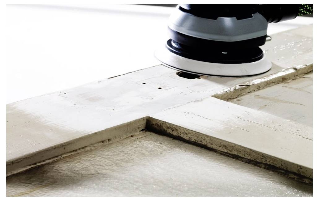 Elektrická bruska vyhlaďuje bílý dřevěný povrch a odstraňuje starou barvu. Tento proces je součástí obnovy nebo renovace.