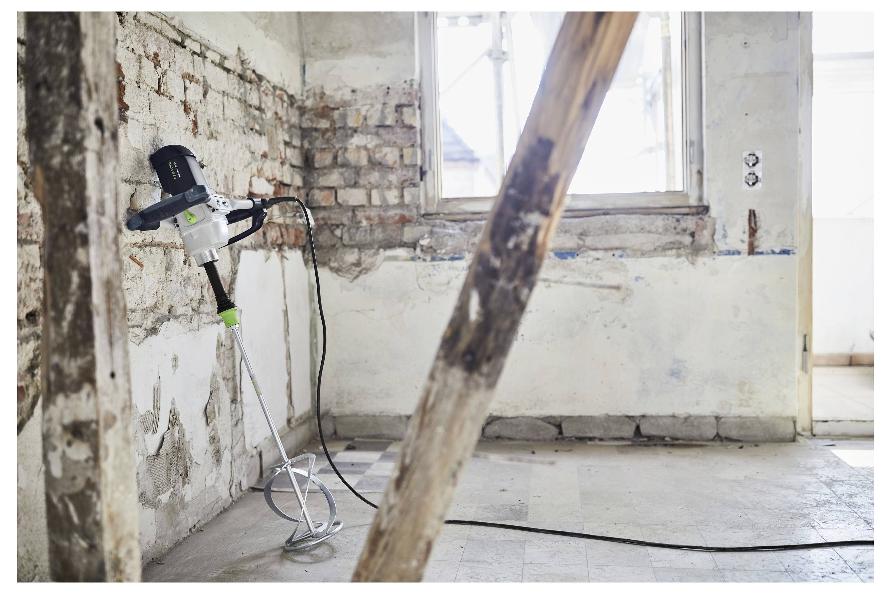 'Prázdná místnost v průběhu renovace s odkrytými cihlami na stěnách a betonovou míchačkou opřenou o zeď. Slunečnímsvětlo se filtruje oknem.'