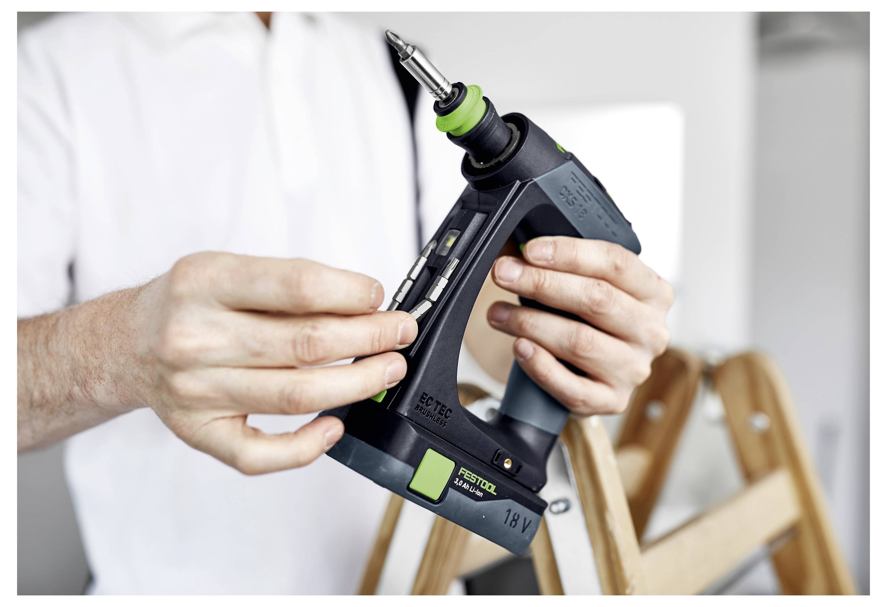 Osoba používá brusku Festool na dřevěném povrchu, přičemž je zdůrazňován ergonomický design nástroje a hadice pro odsávání prachu pro účinné broušení.