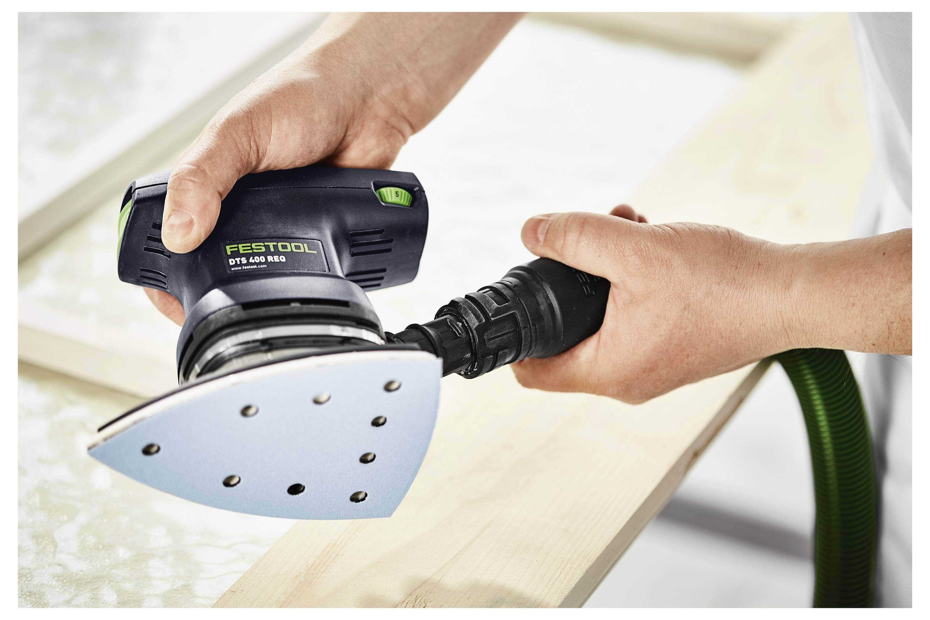 Ruce používající brusku Festool DTS 400 na dřevěném povrchu, zdůrazňující ergonomický design tohoto nástroje a efektivnost při hladění dřeva.