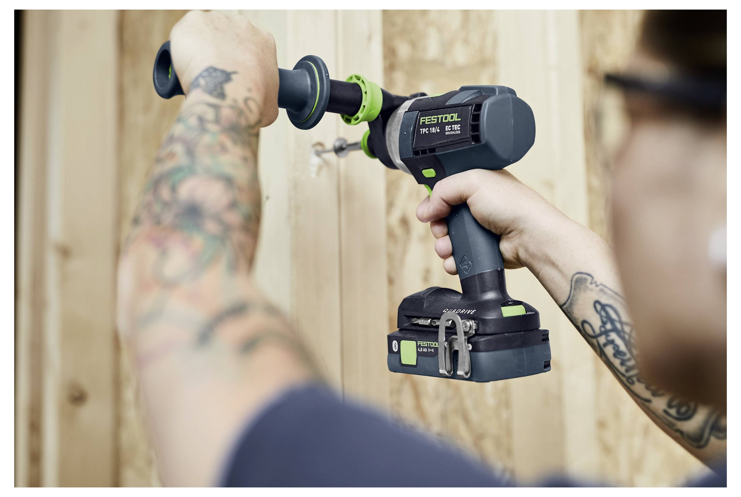 Osoba používající Festool elektrické nářadí k vrtání do dřeva, ukazující tetování na rukou.
