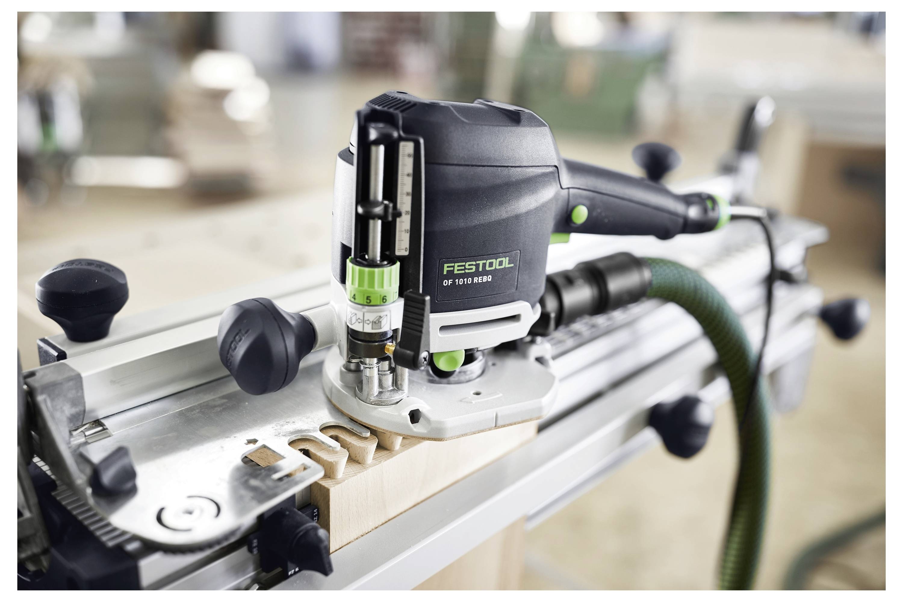 Frézka Festool OF 1010 EBQ-Plus používaná na dřevěném obrobku s přesnými řezy podél vodící lišty, umístěná v prostředí dílny.