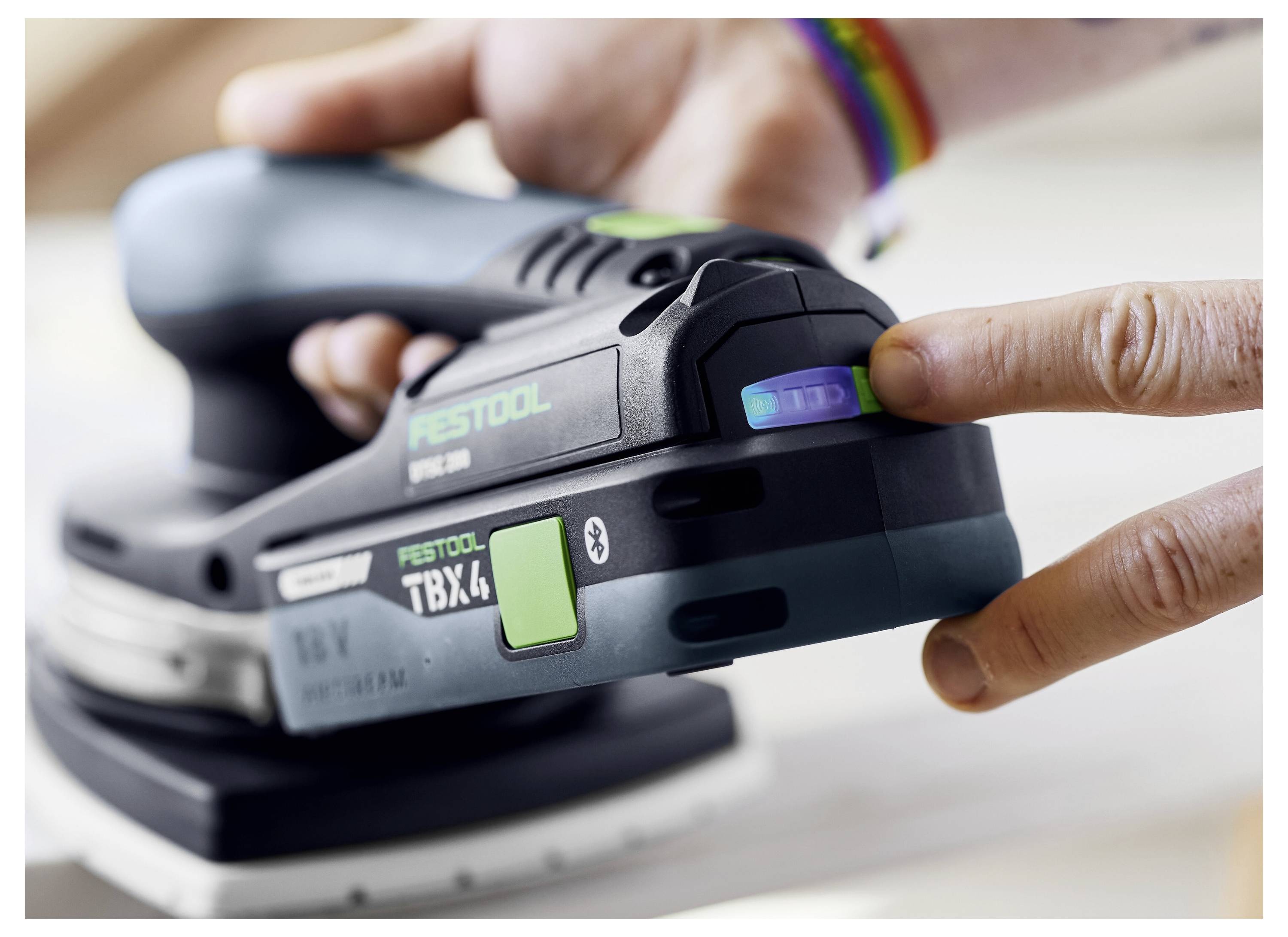 Ruka osoby nastavuje ciferník rychlosti na brusce Festool TBX 4, přičemž zvýrazňuje moderní design a ovládací prvky nářadí.