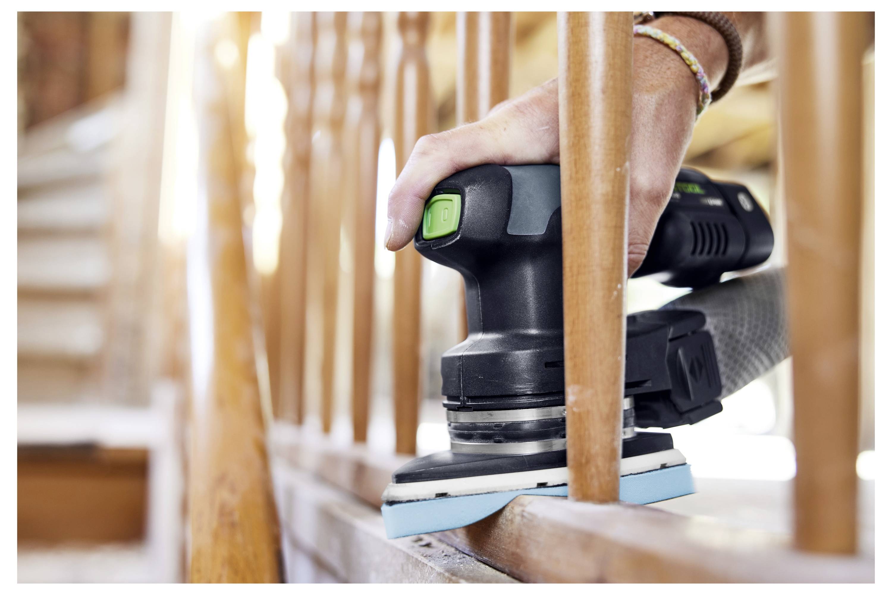 Ruka brousící dřevěné zábradlí elektrickým bruskou, vyhlazující povrch dřeva, zdůrazňující proces renovace.