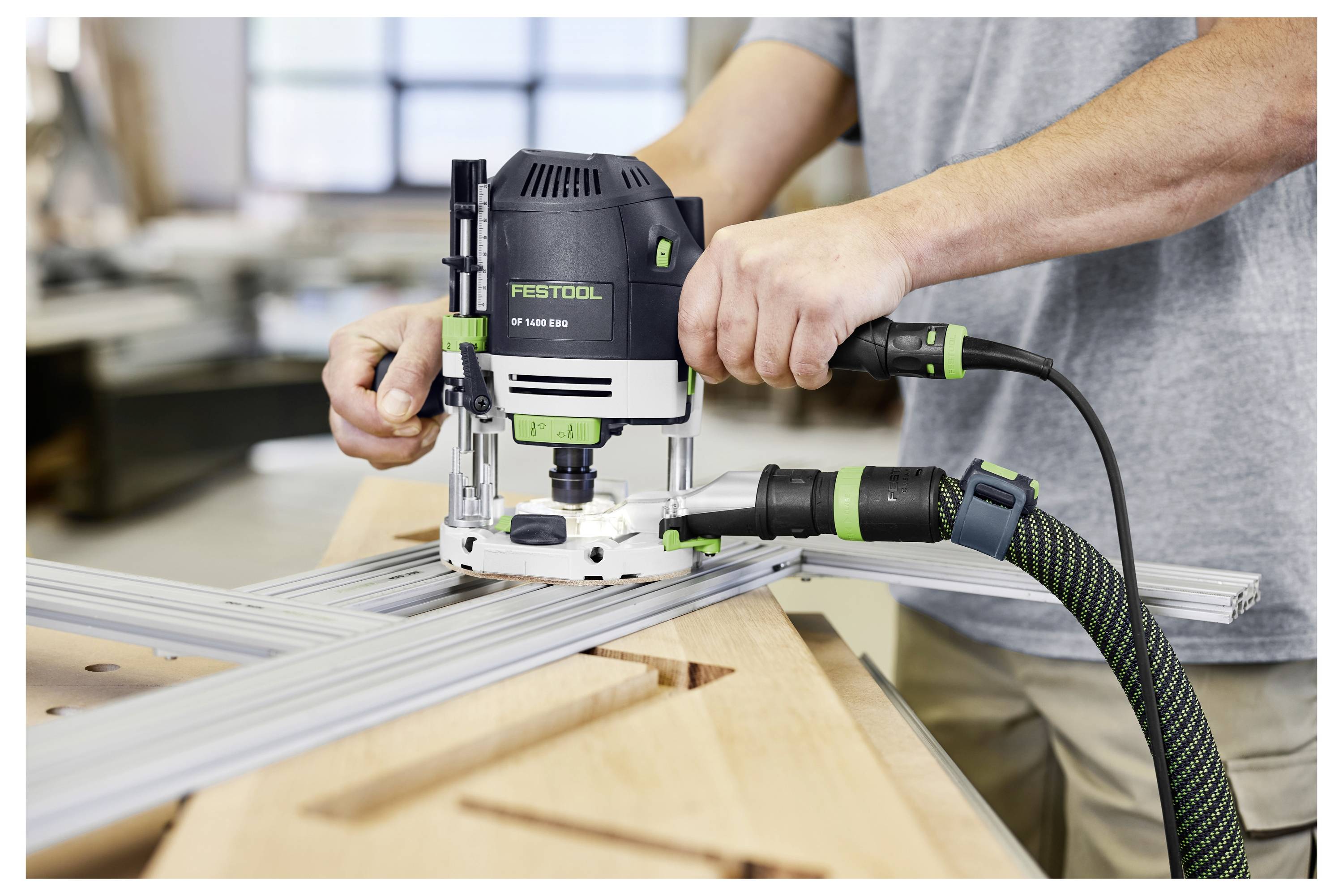 Osoba používá frézovací stroj na vytváření přesných drážek v dřevěné desce na pracovní stůl. Nástroj je označen značkou "Festool".