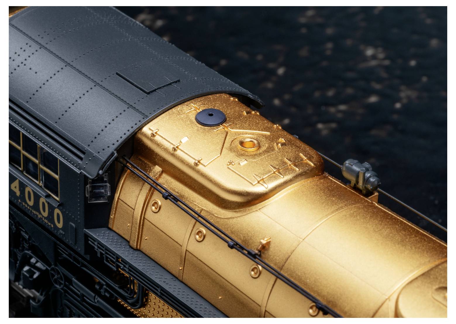 Detailní záběr na modelový parní stroj v černé a metalické zlaté barvě, který vykazuje složité textury a značky s číslem 4000.
