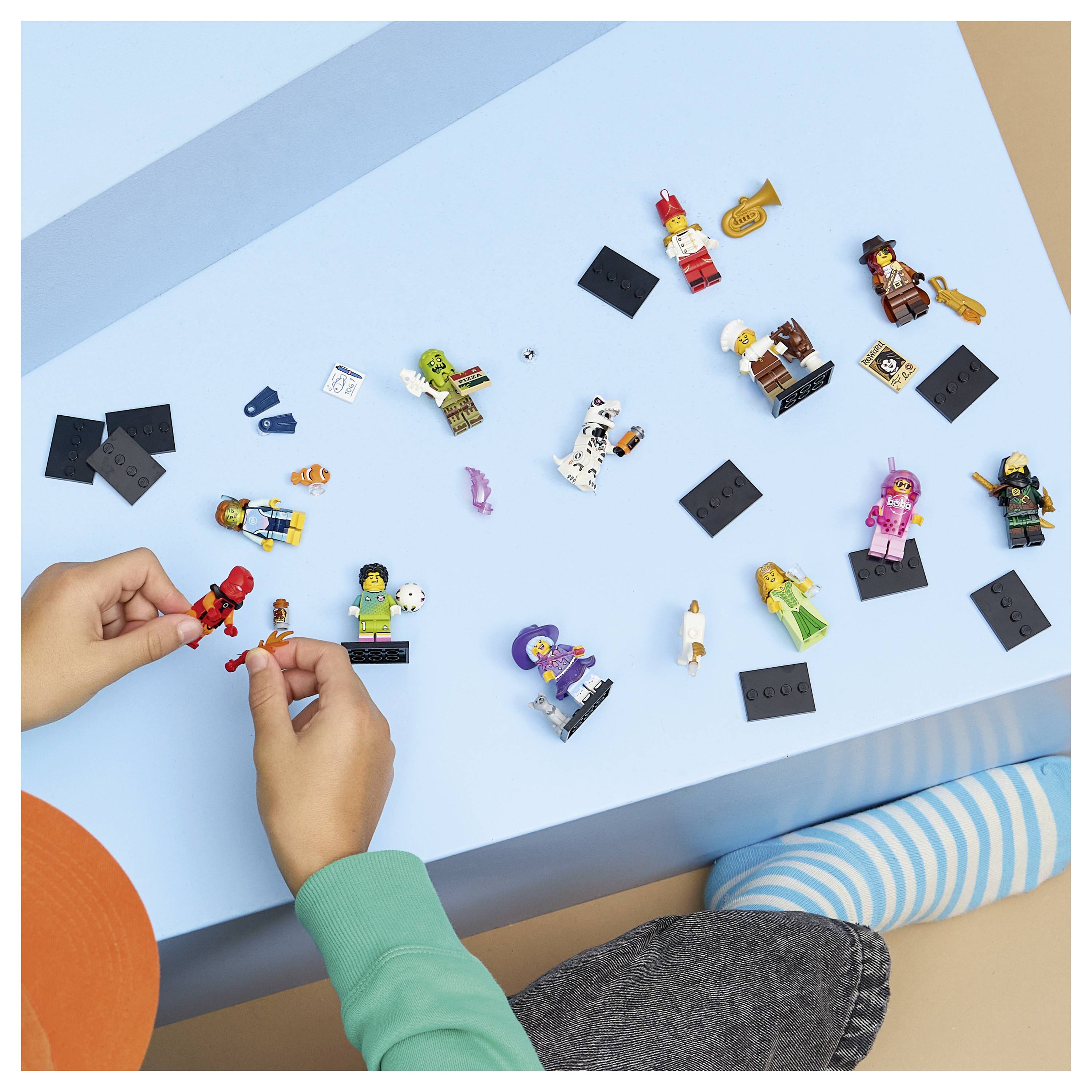 Dítě skládající a uspořádávající LEGO minifigurky a součástky na modrém stole, s několika figurkami rozptýlenými kolem.