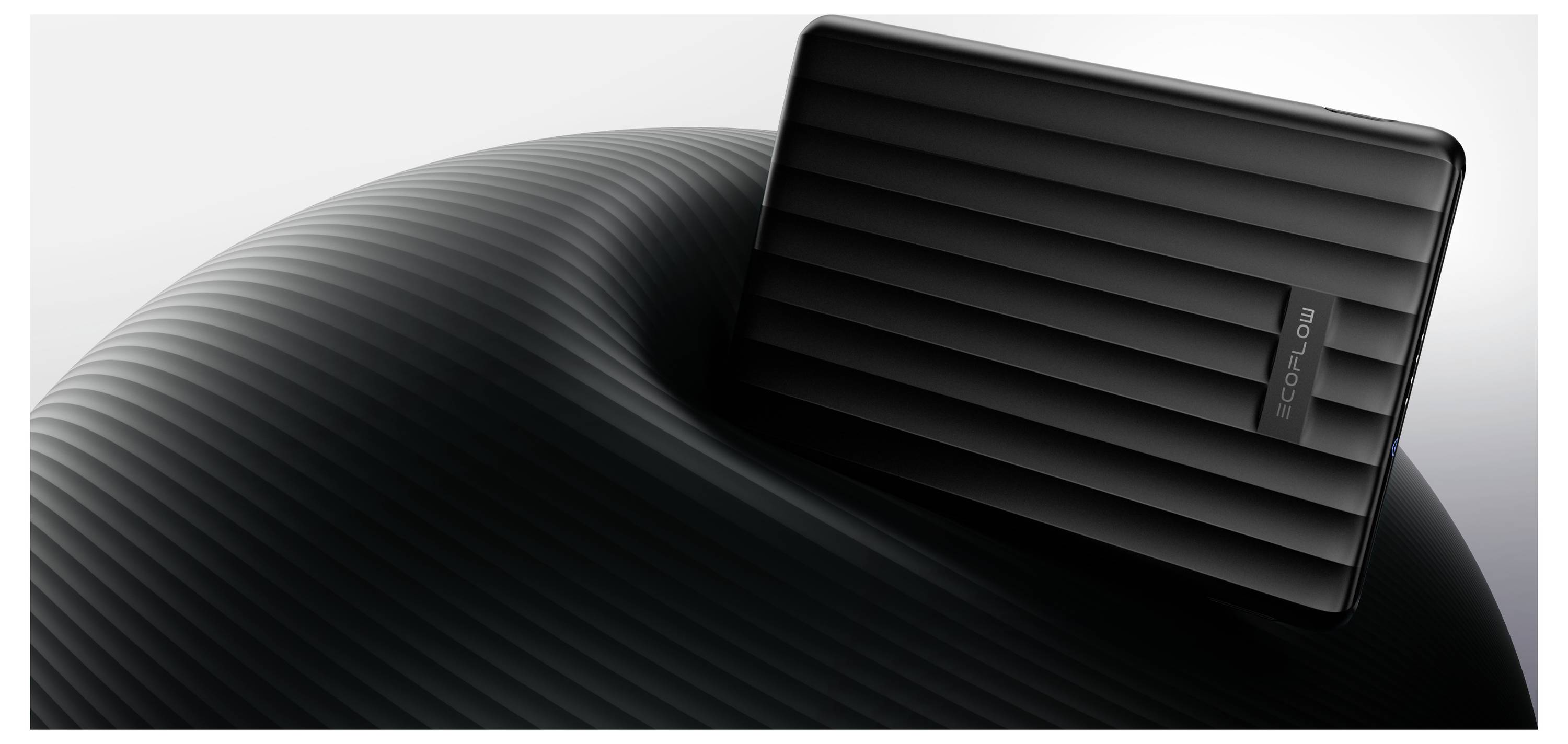 Černý, pruhovaný pevný disk spočívá na zakřivené, vroubkované ploše před světlým pozadím a vykazuje svůj elegantní, moderní design.