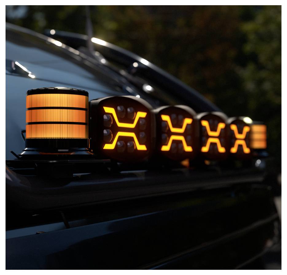 Detailní záběr na svetelnou lištu střechy vozidla se svítícími oranžovými varovnými světly a osvětlenými X-tvarovanými signály, fotografovaný v půl temna.