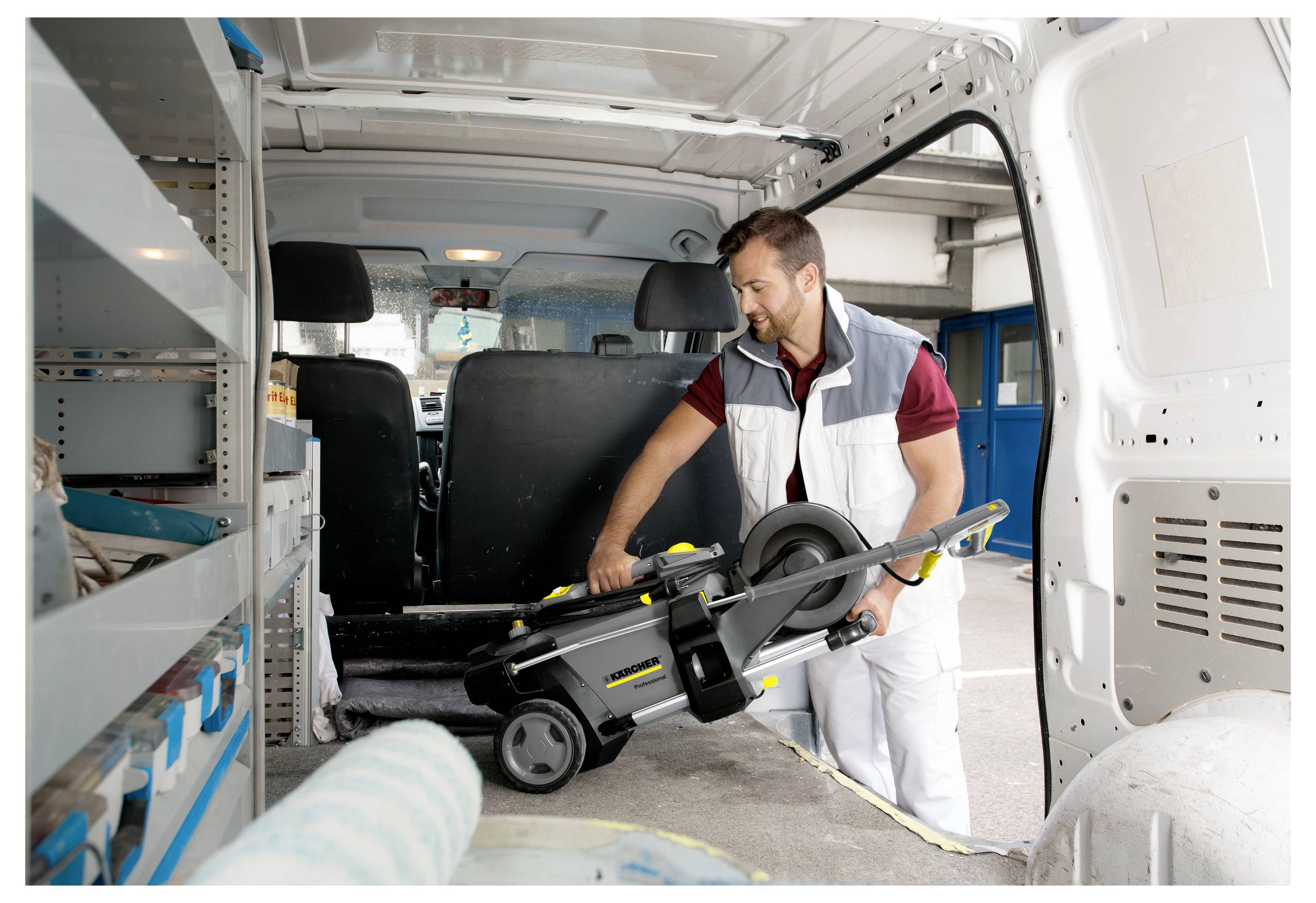Osoba nakládá pokosovou pilu do zadní části pracovního vozu, přičemž se připravuje na stavební nebo opravárenskou práci.