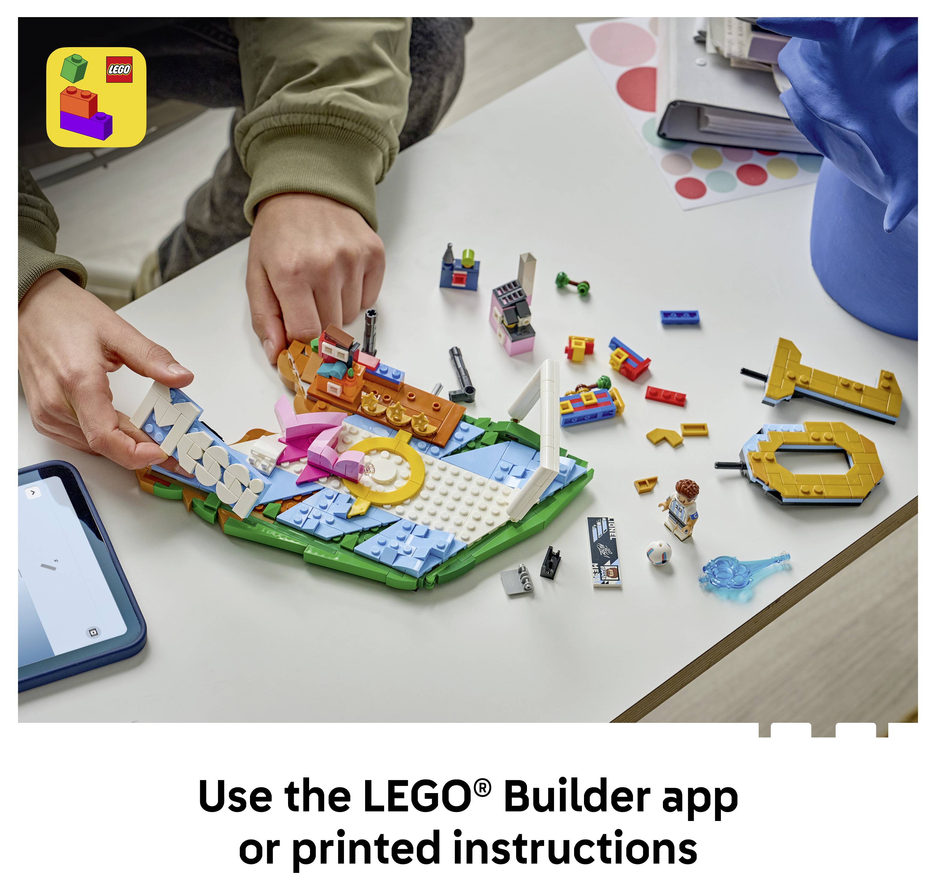 Ruce skládající LEGO sadu na stole, s viditelnými aplikací telefonu a textem "Používejte aplikaci LEGO® Builder nebo tištěné pokyny".