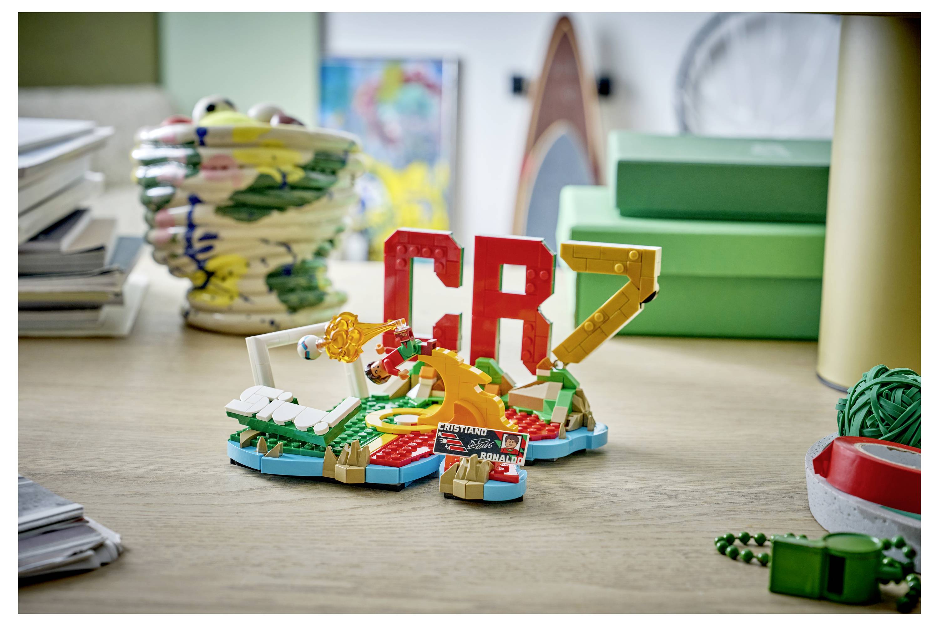 LEGO stavba na stole se slovy „CR7" s fotbalovou minifigurkou v diorámu, obklopená pomůckami na tvorbu a krabicemi.
