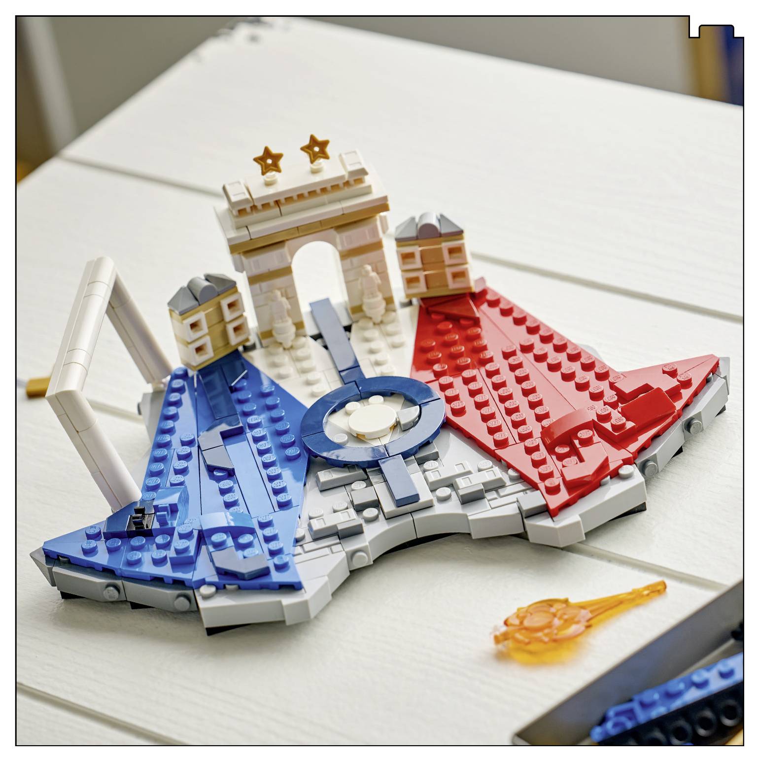 LEGO-stylový model stadionu nebo arény s modrými a červenými sekcemi, centrálním kruhovým prvkem a obloukem s hvězdami na bílém stole.
