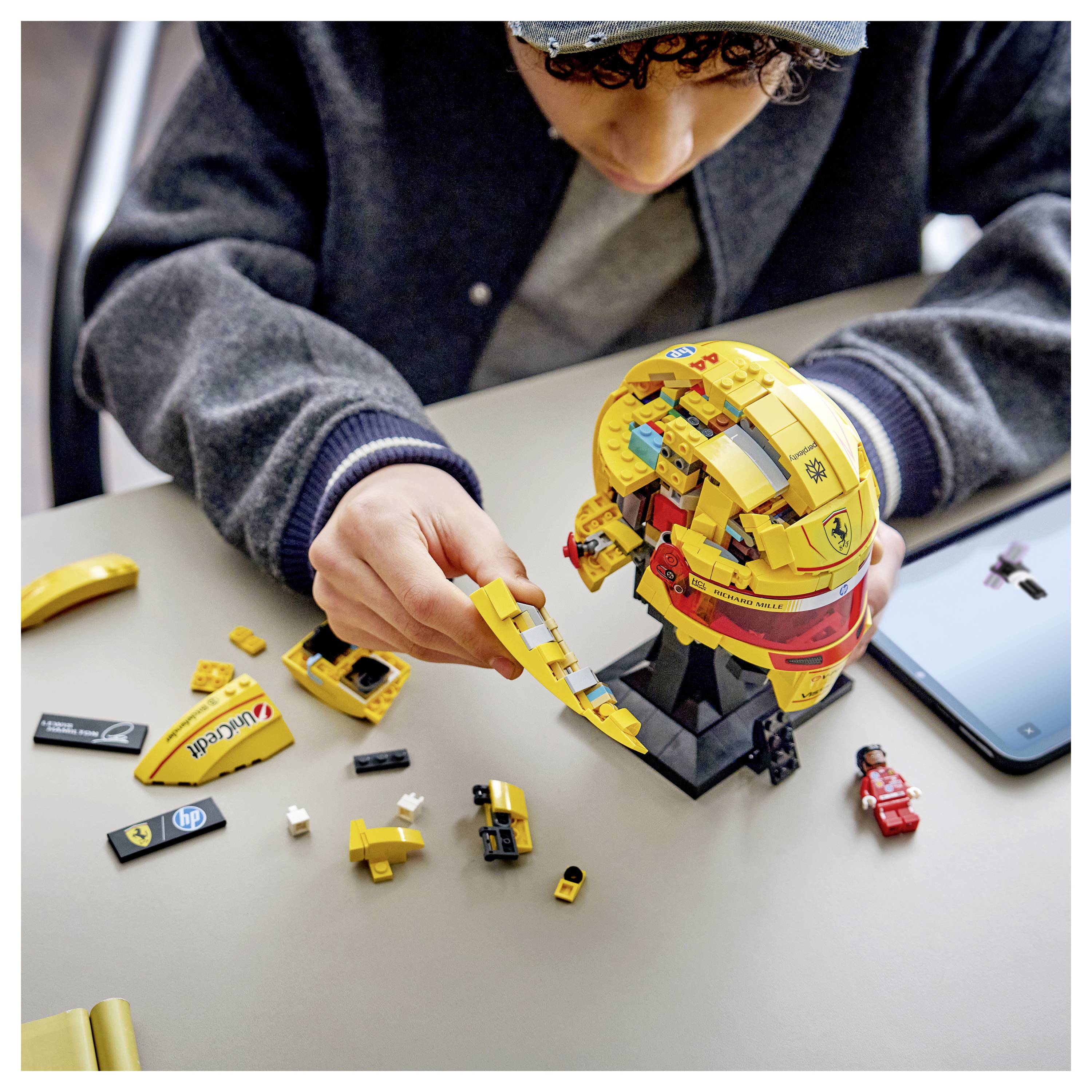Osoba skládá žlutý LEGO glóbus na stole, obklopen LEGO kostičkami a červenou minifigurkou, což naznačuje stavební aktivitu.