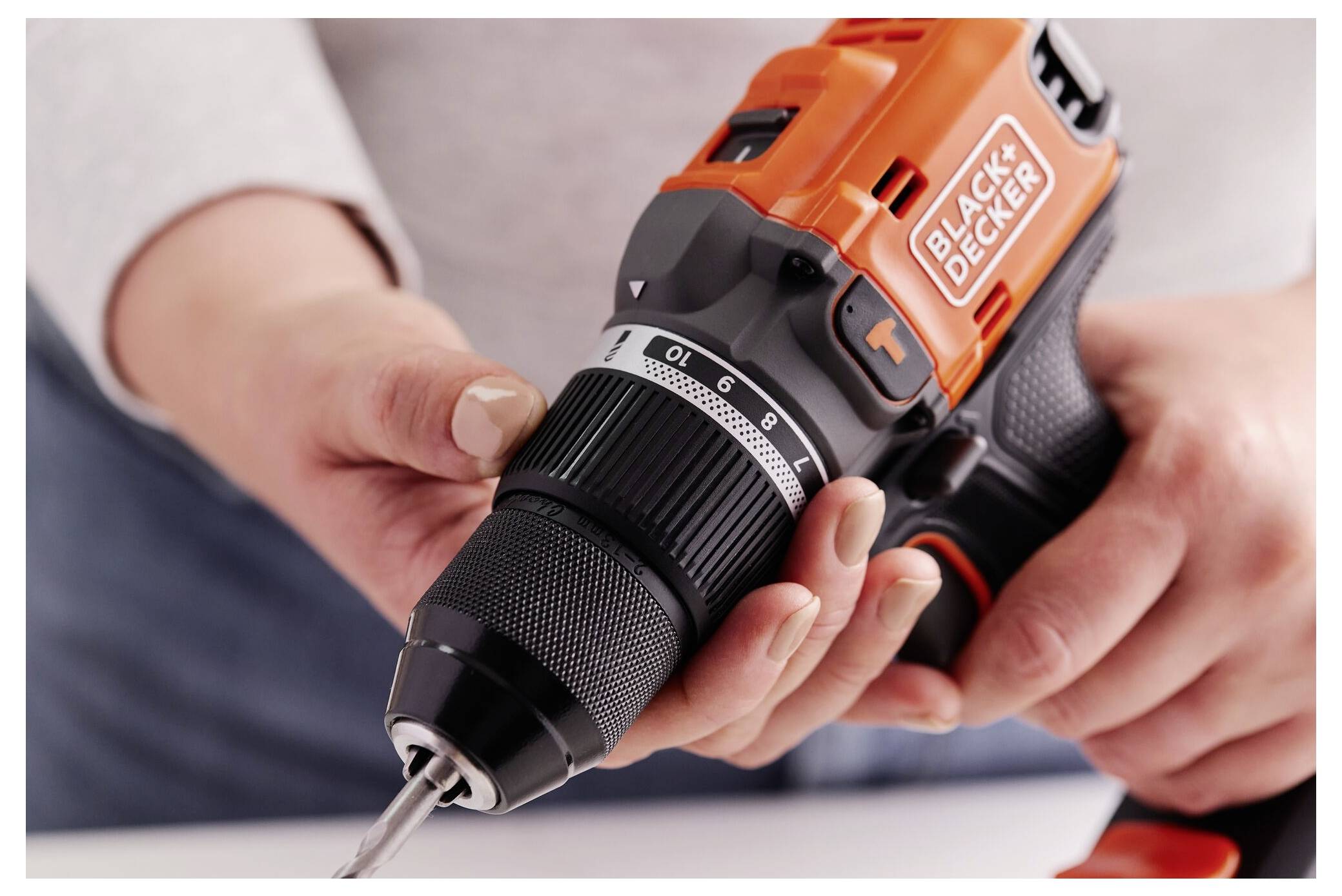 Osoba drží oranžovo-černou bezdrátovou akumulátorovou vrtačku značky 'BLACK+DECKER' a soustředí se na připojovaný vrták.