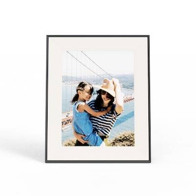 Rámeček s fotografií zobrazuje osobu v klobouku drženou dítě, v pozadí je vidět most Golden Gate v slunečný den.