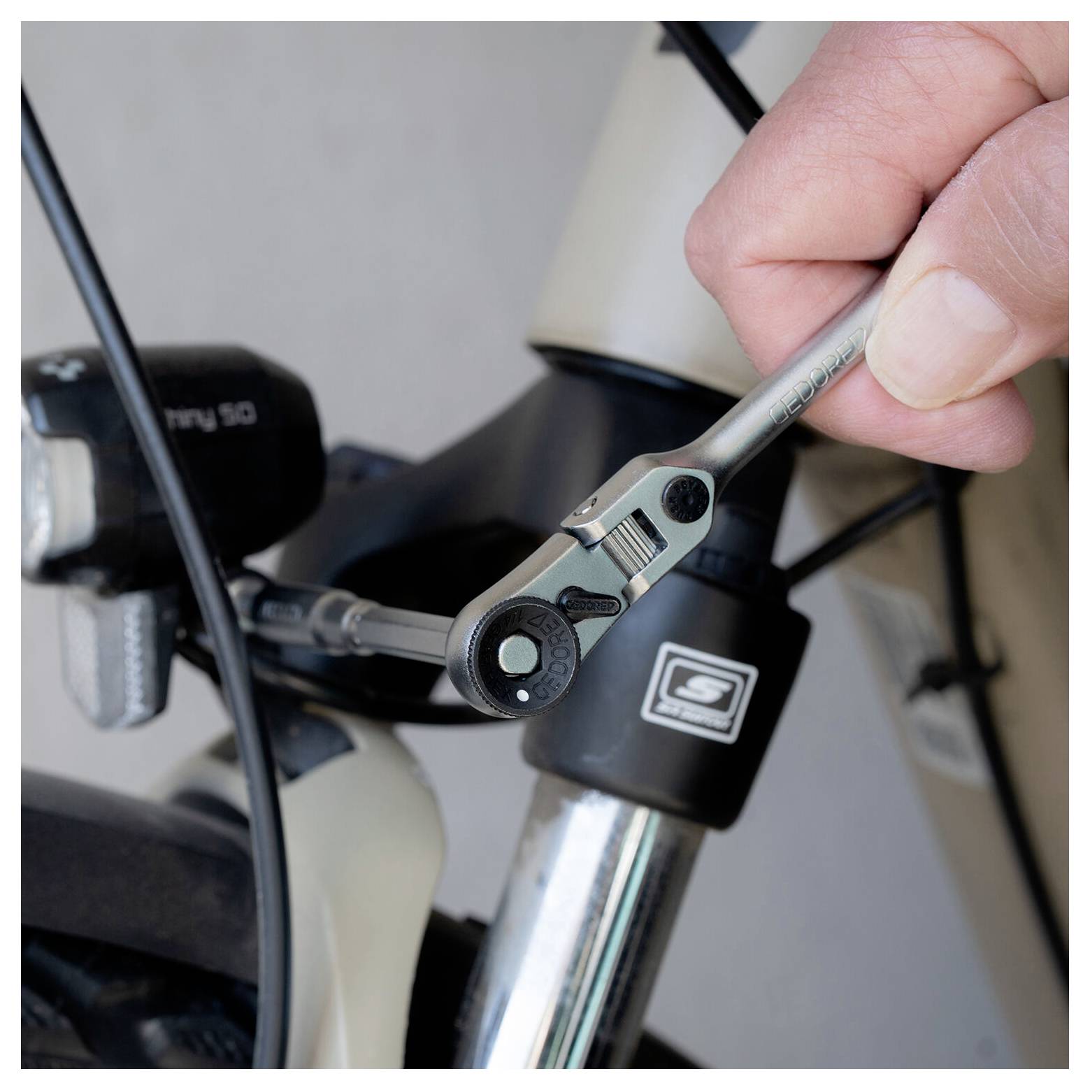 Detailní záběr na ruku používající klíč k úpravě šroubu bicyklového kabelu poblíž přední vidlice a brzdového systému.