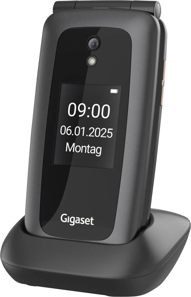 Digitální displej zobrazuje datum "06.01.2025" a čas "09:00" na zavřeném klapkovém telefonu stojícím v nabíjecím stojanu.