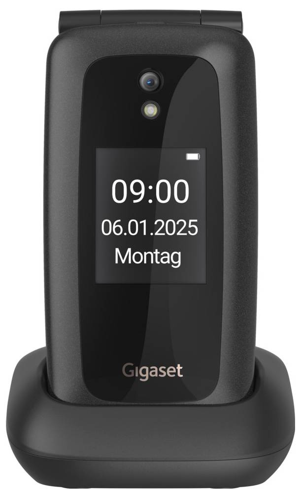 Černý skládací telefon na stojanu na nabíjení zobrazuje na displeji „09:00", „06.01.2025", „Pondělí".