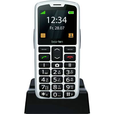 Černý a bílý mobilní telefon s velkými tlačítky na nabíjecím stojanu. Displej zobrazuje „12:34 Pá 28.07" s ikonami pro zprávy a kontakty.