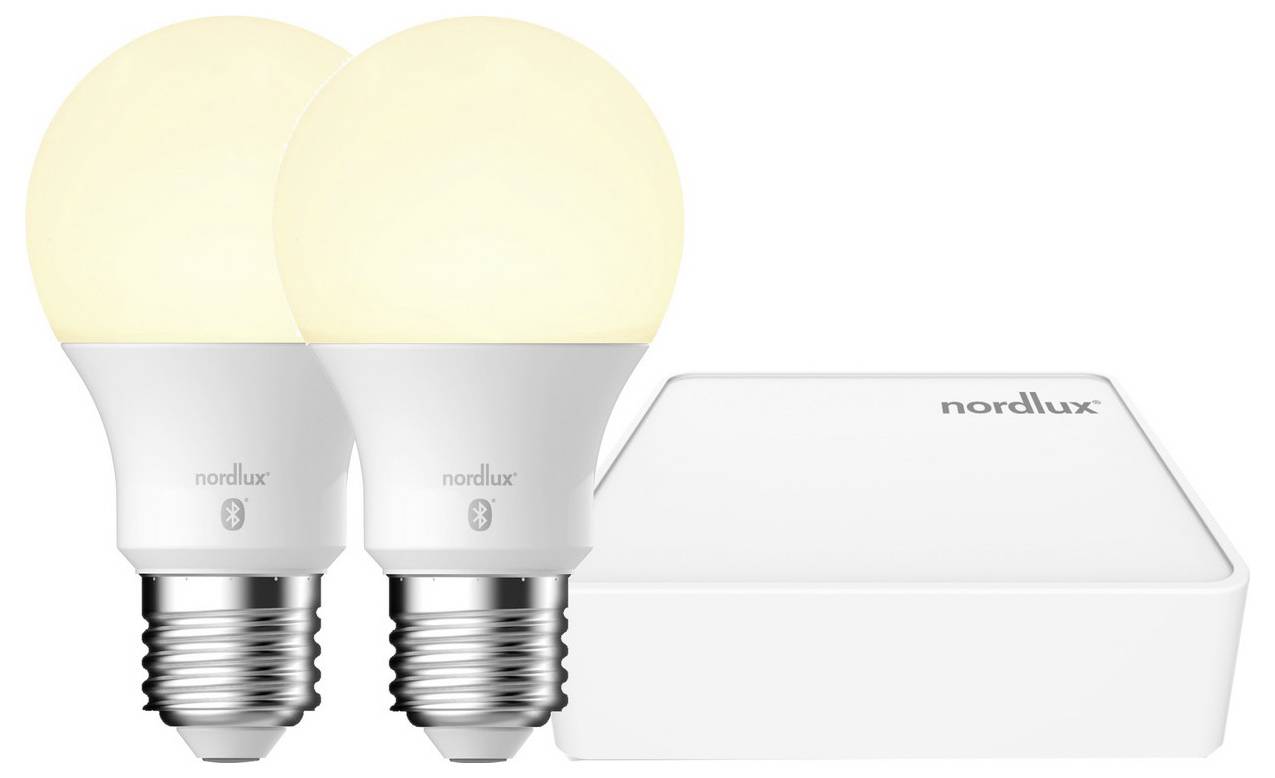 Jsou zobrazeny dvě inteligentní LED žárovky Nordlux a hub Nordlux. Žárovky mají standardní závitový závěs a vyzařují teplé světlo. Hub je kompaktní s minimálním designem.