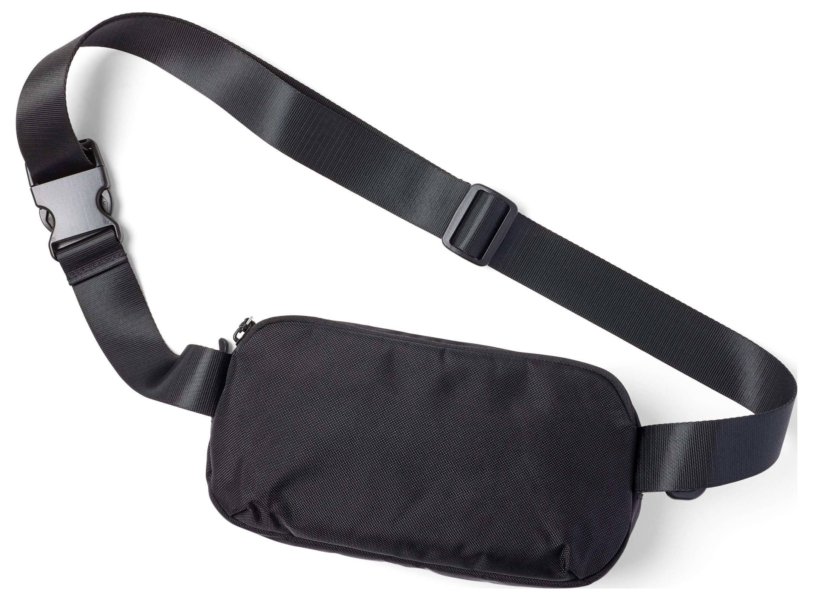 Černá crossbody taška s nastavitelným nylonový páskem a spínáním na přezku na bílém pozadí.