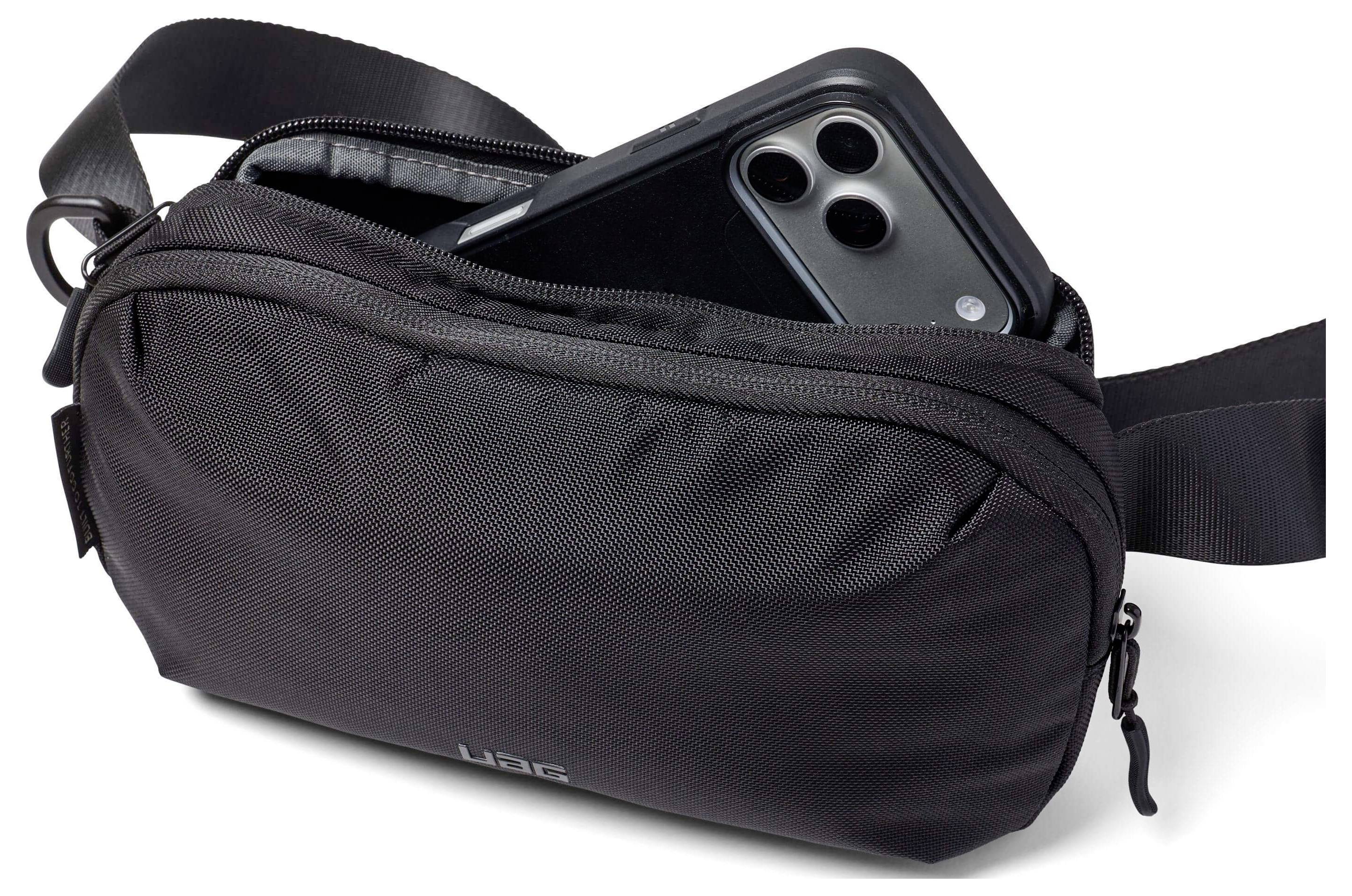 Černá crossbody taška s částečně otevřeným zipem odhaluje smartphone uvnitř, což předvádí schopnost tašky skladovat věci.
