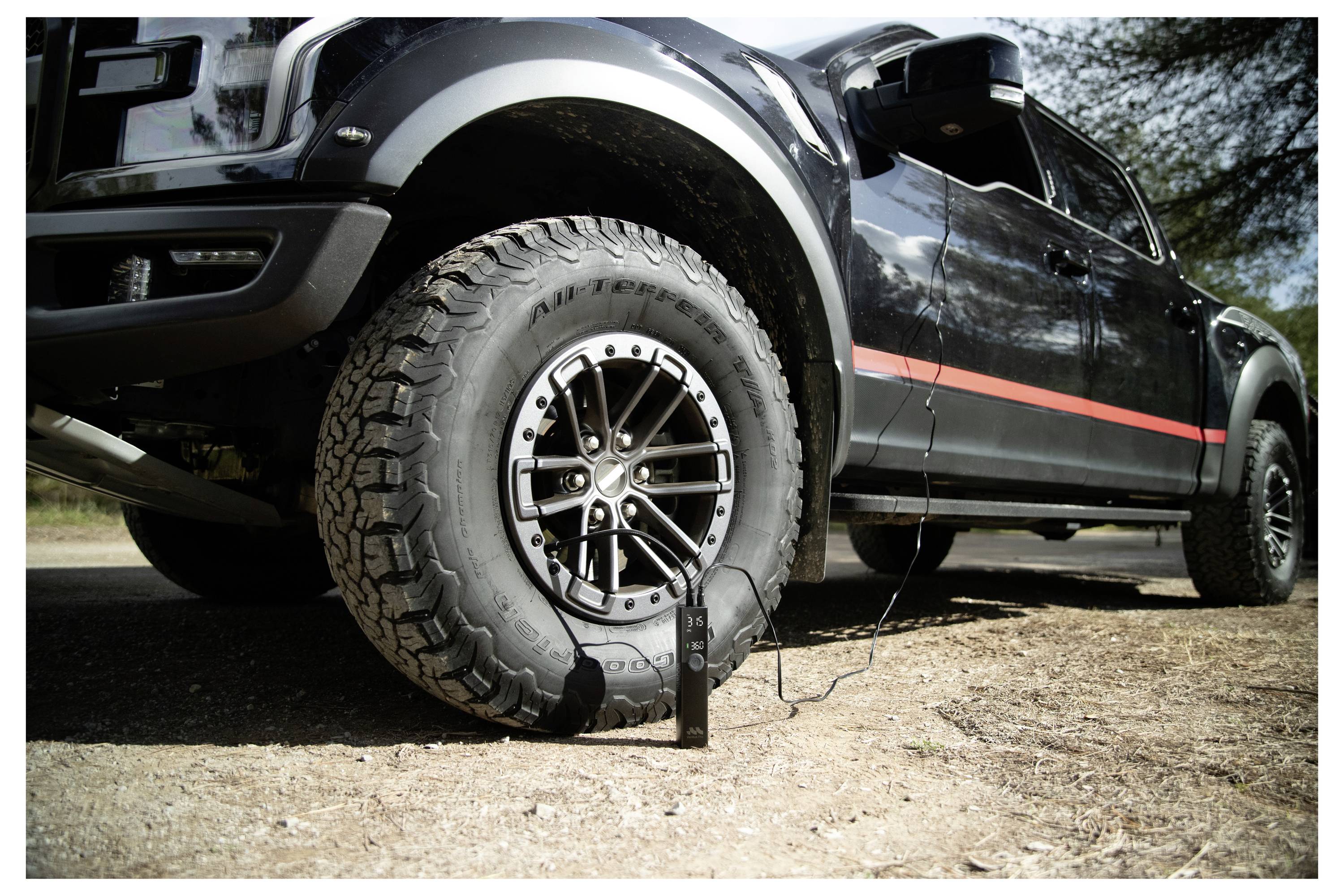 Černý terénní pick-up s defektní přední pneumatikou; malá vzduchová pumpa je připojena hadicí k nahušťování pneumatiky.