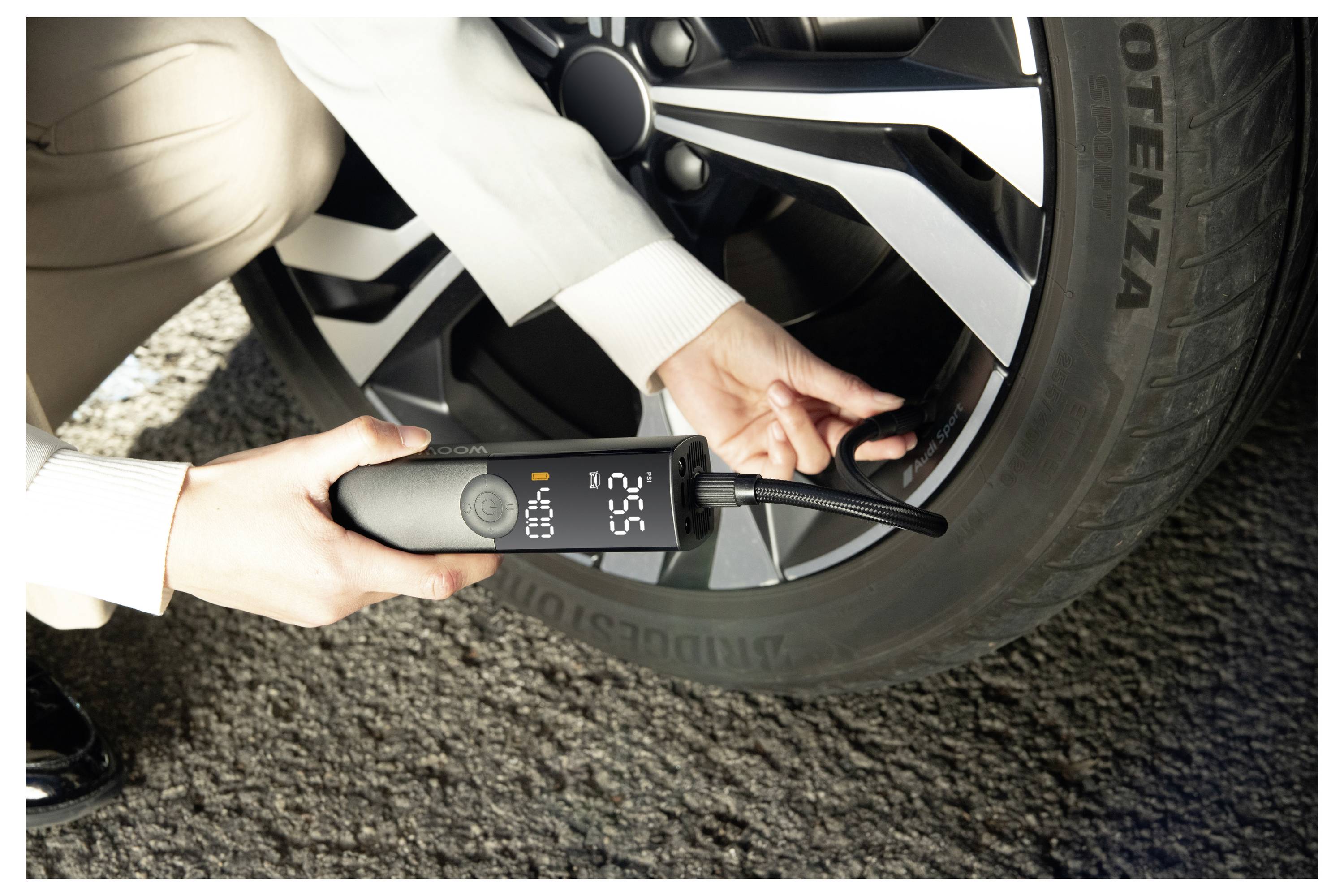 Osoba používající digitální tlakomer na pneumatiky ke kontrole tlaku v pneumatice automobilu, přičemž displej ukazuje přibližně 2,65 bar.