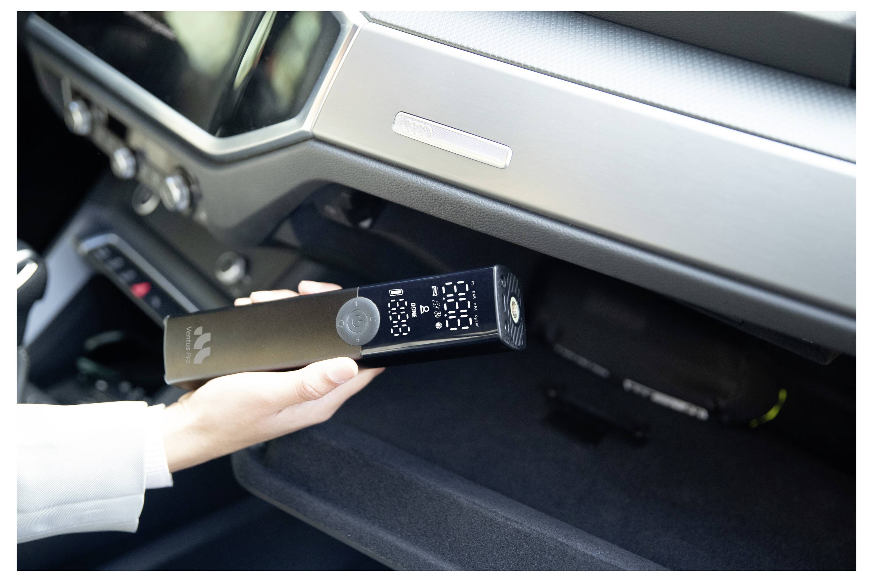 Ruka umisťující černé elektronické zařízení do přihrádky na rukavice nebo úložného prostoru v palubní desce automobilu.