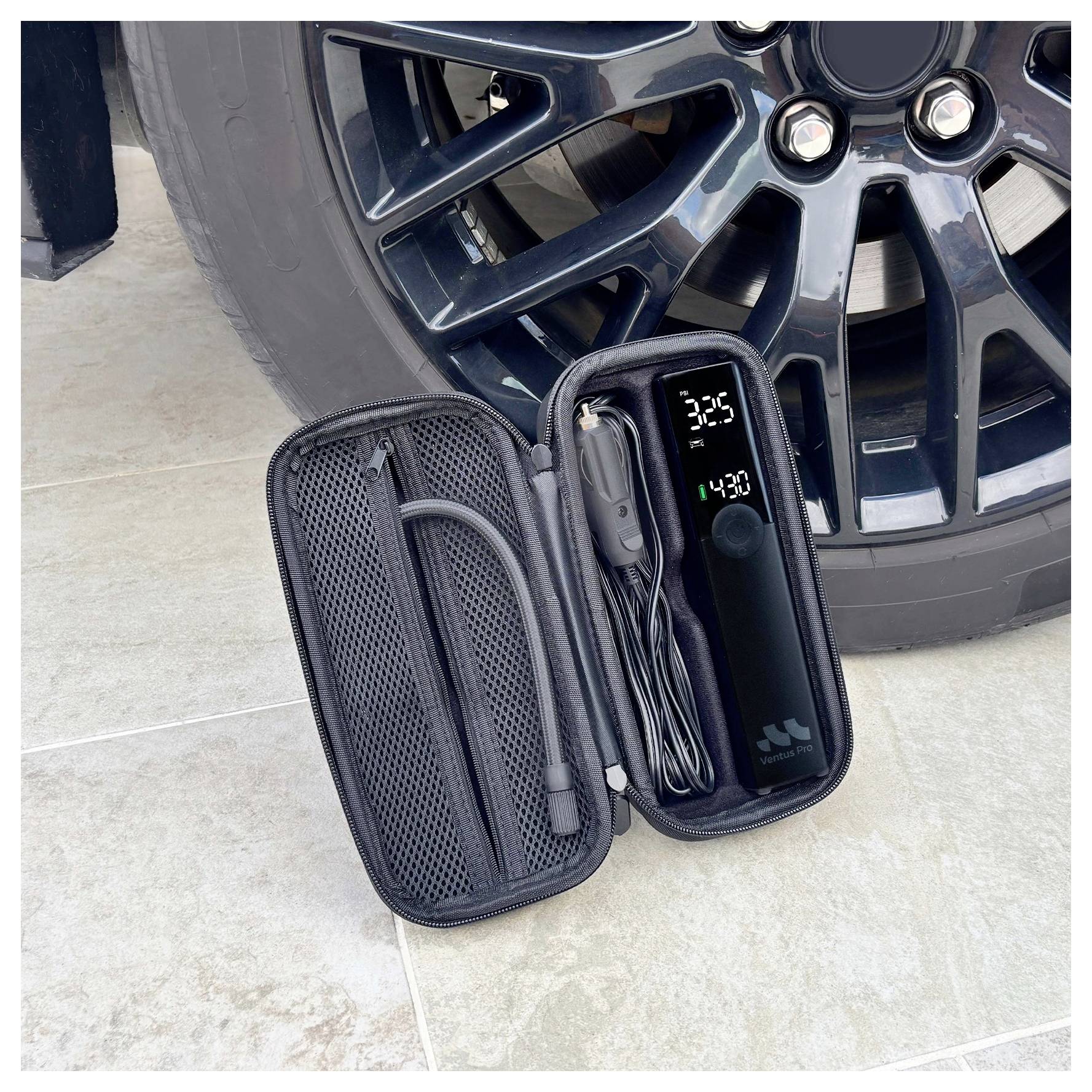 Přenosný set pro huštění pneumatik otevřený vedle automobilového kola, zobrazující pumpu, hadici a digitální displej tlaku.
